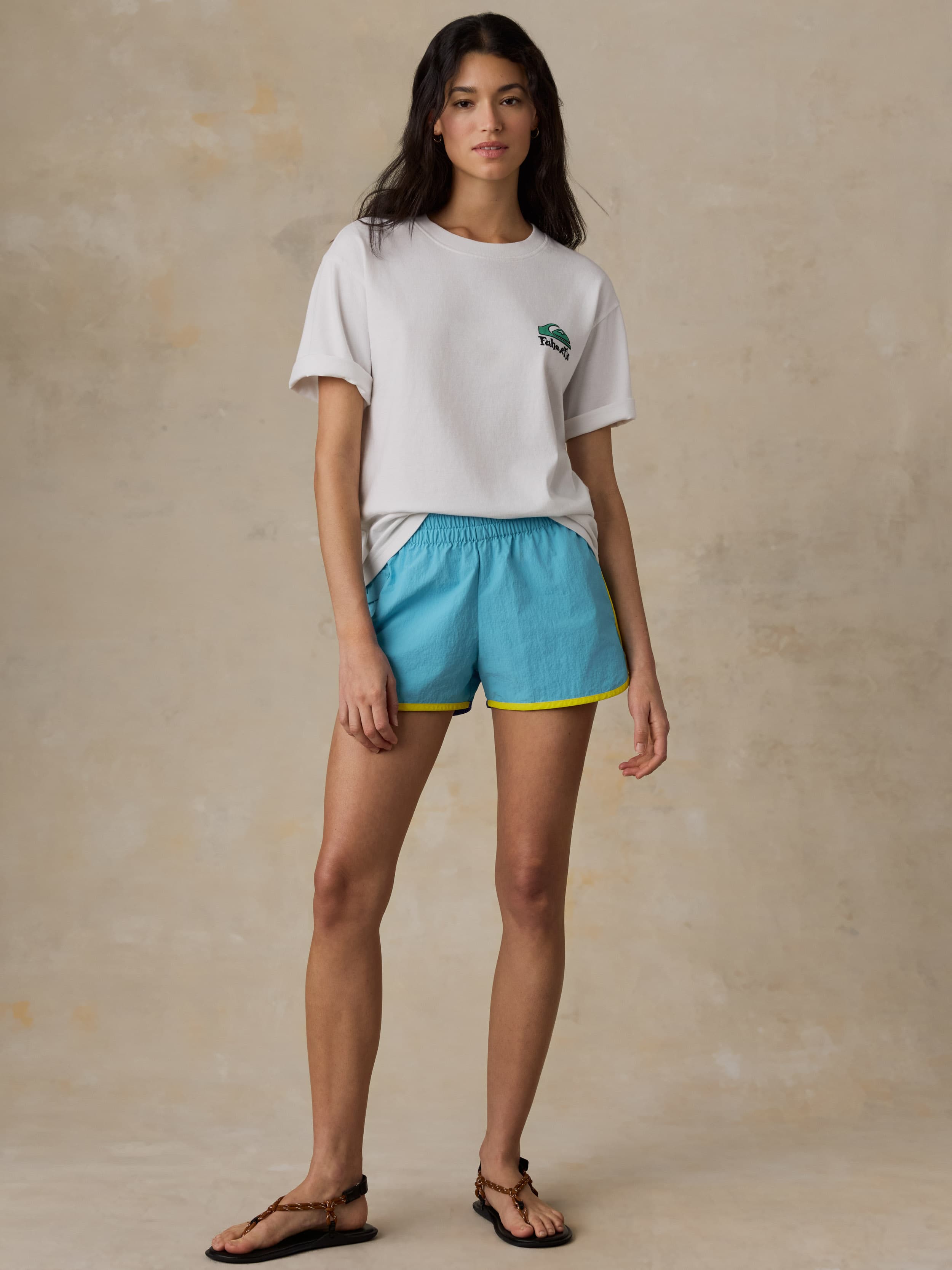 Woman wearing a white t-shirt with a logo and blue shorts on a beige background