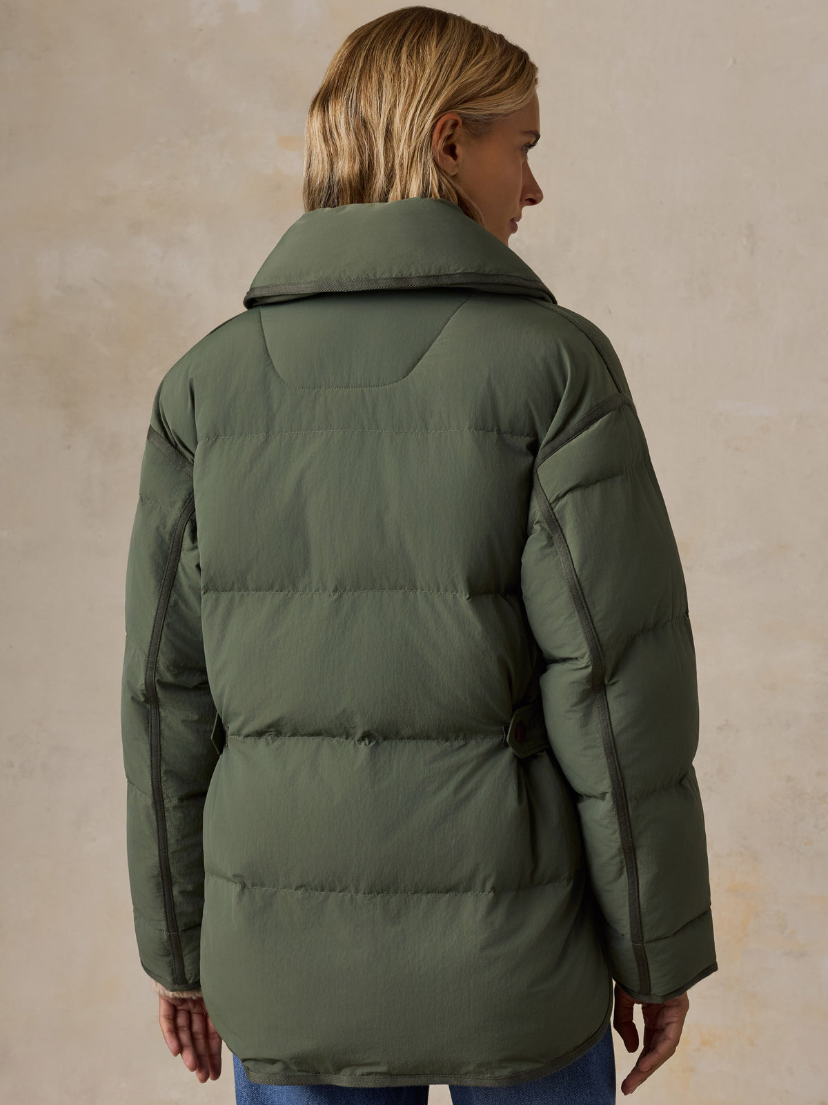 A woman viewed from the back wearing a green jacket and blue jeans, image 2 of 7