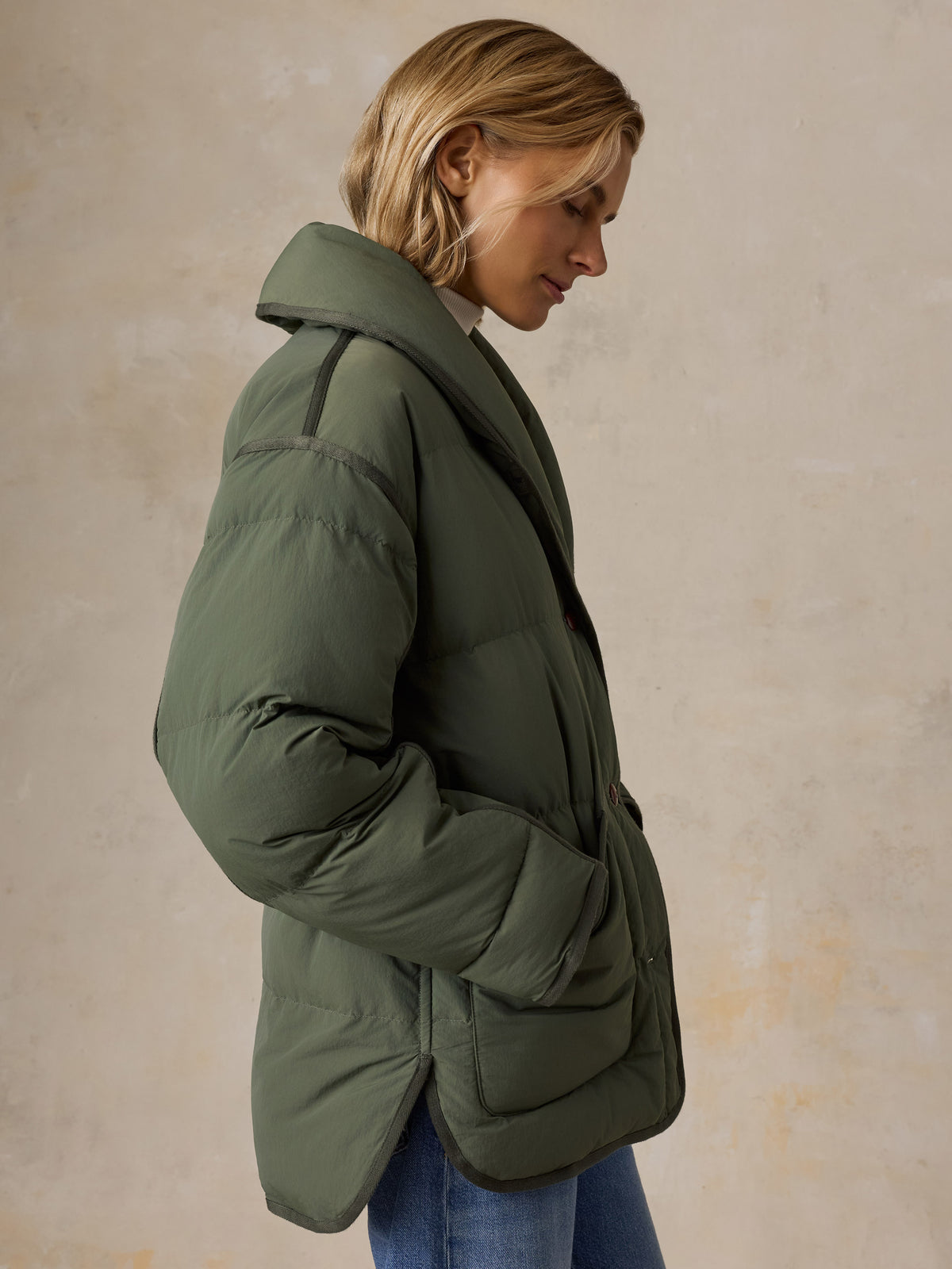 A woman wearing a green jacket and blue jeans, image 6 of 7