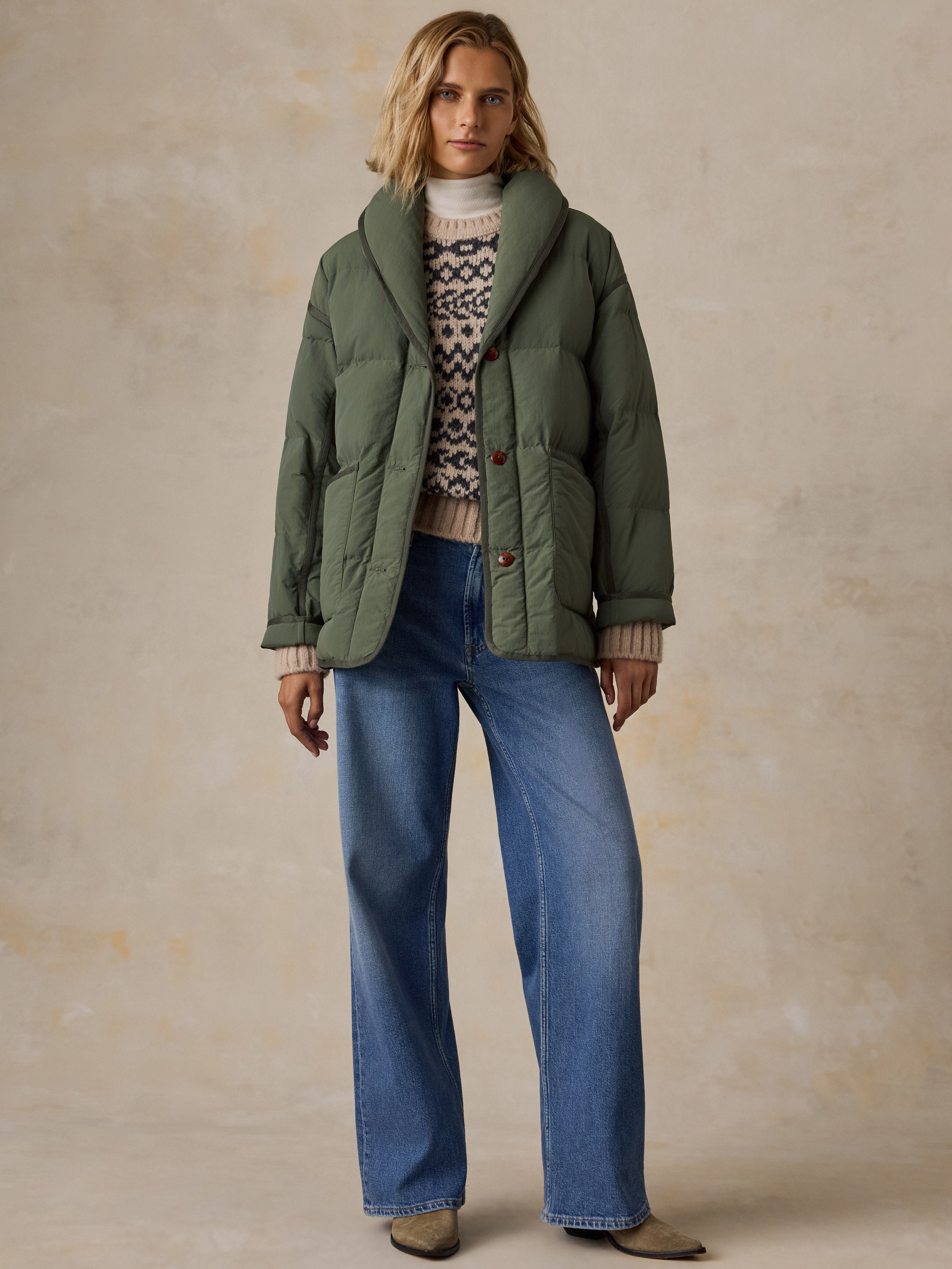 A woman wearing a green jacket over a knit sweater and blue jeans