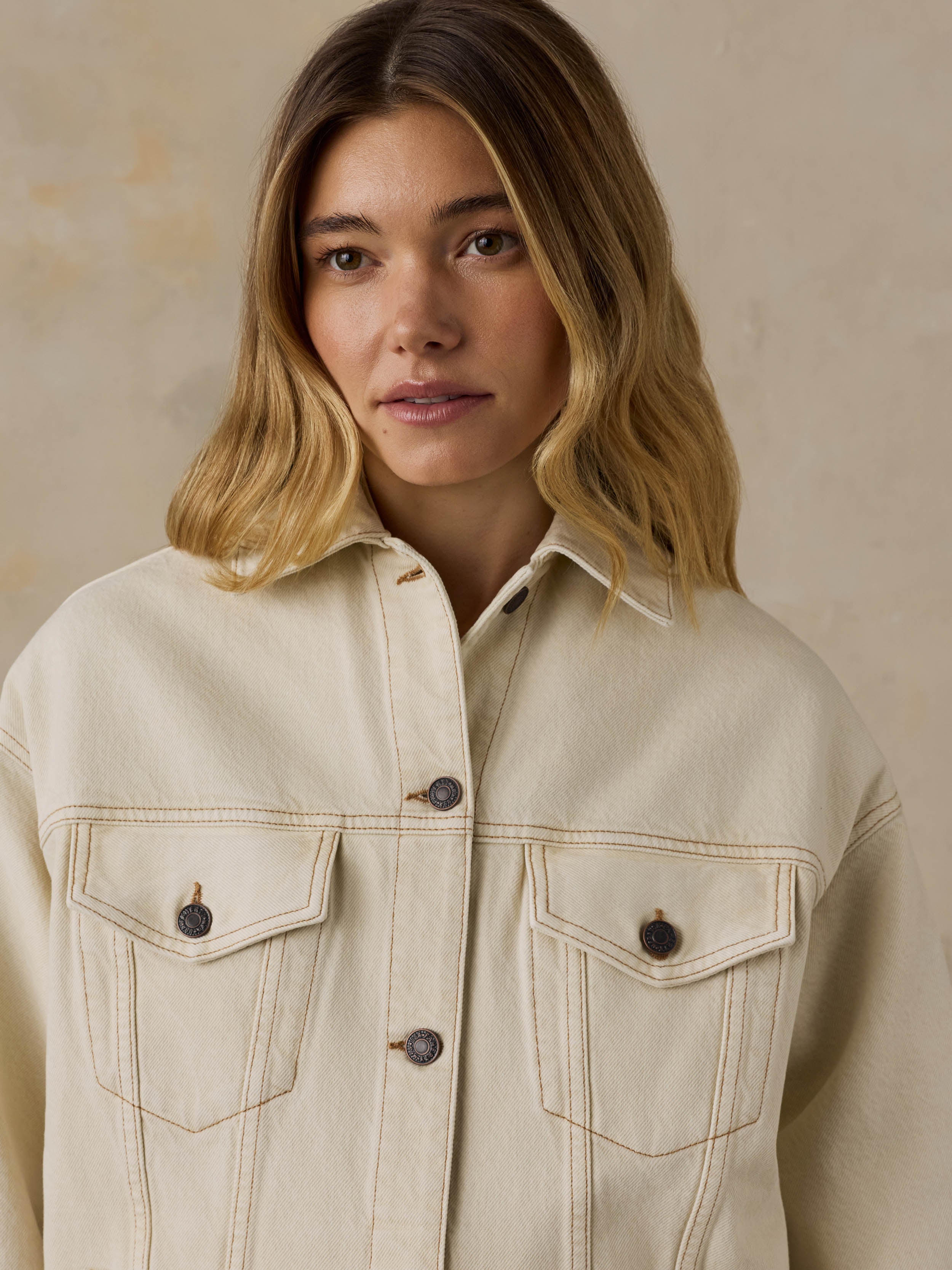 Woman wearing an off white denim jacket against a beige background
