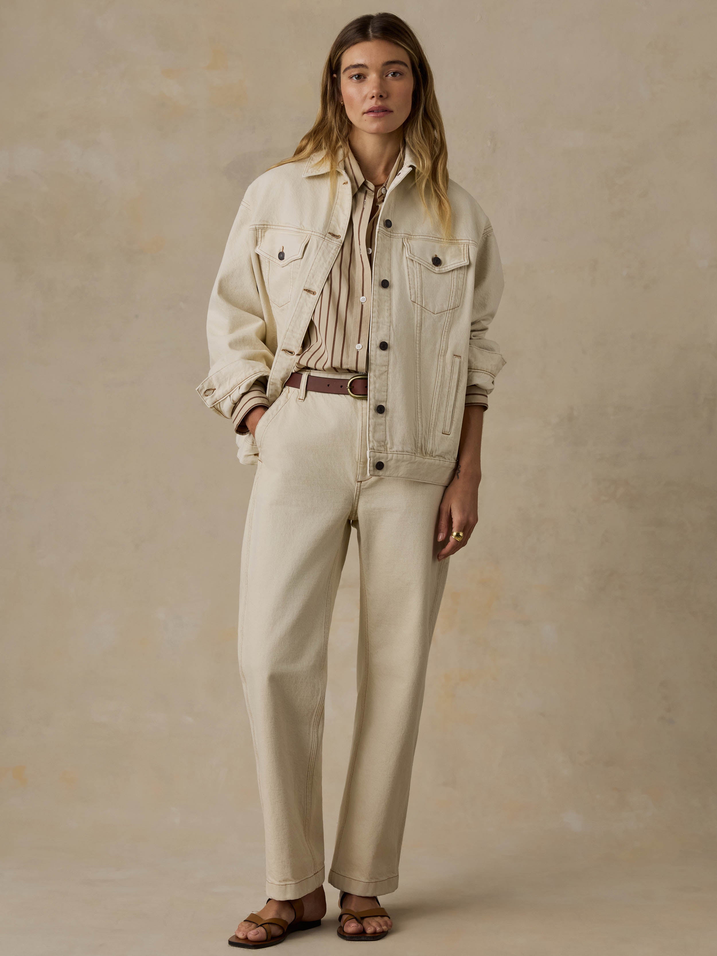 Woman wearing an off white denim jacket and pants against a beige background