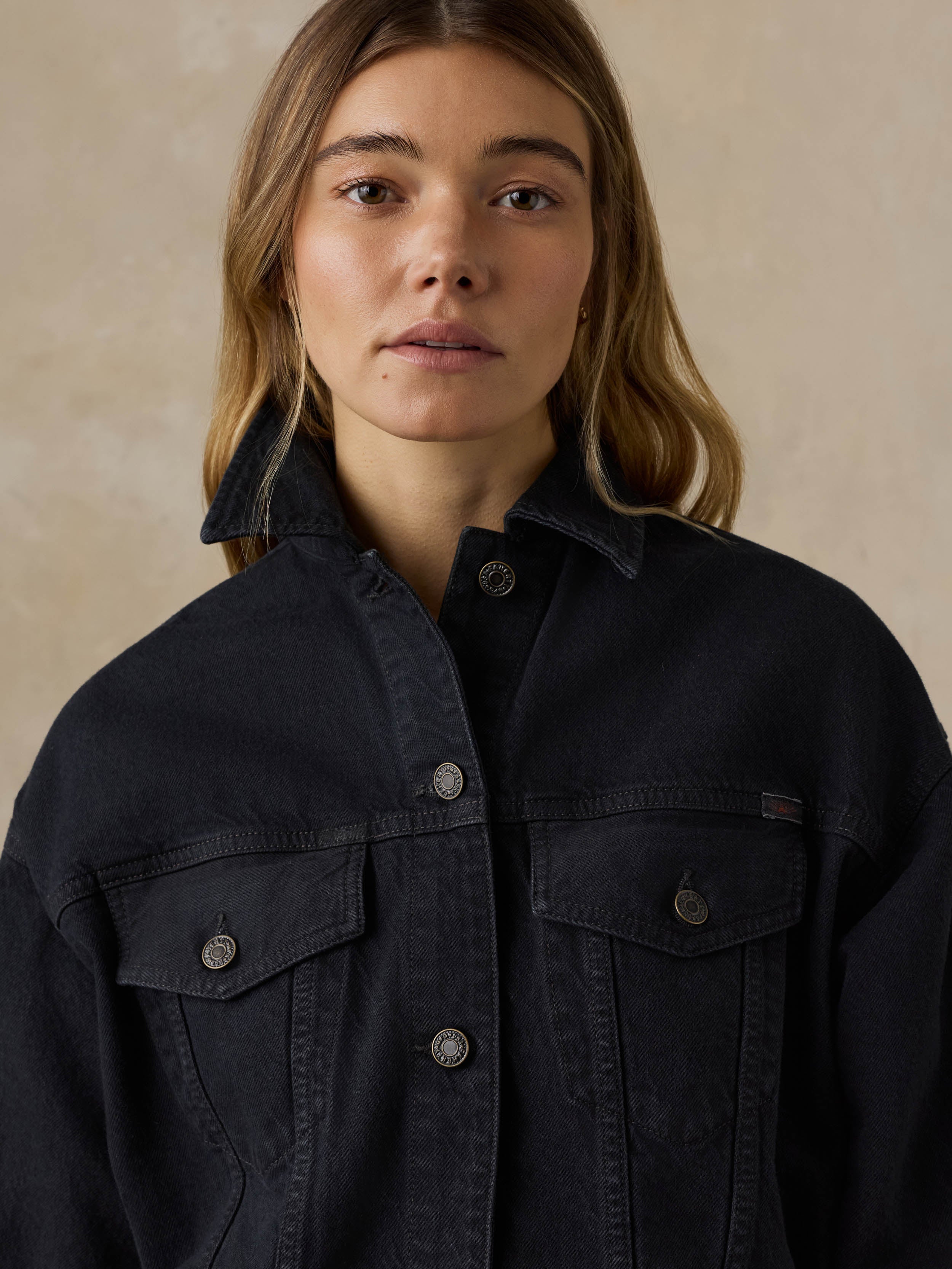 Woman wearing a black denim jacket against a beige background