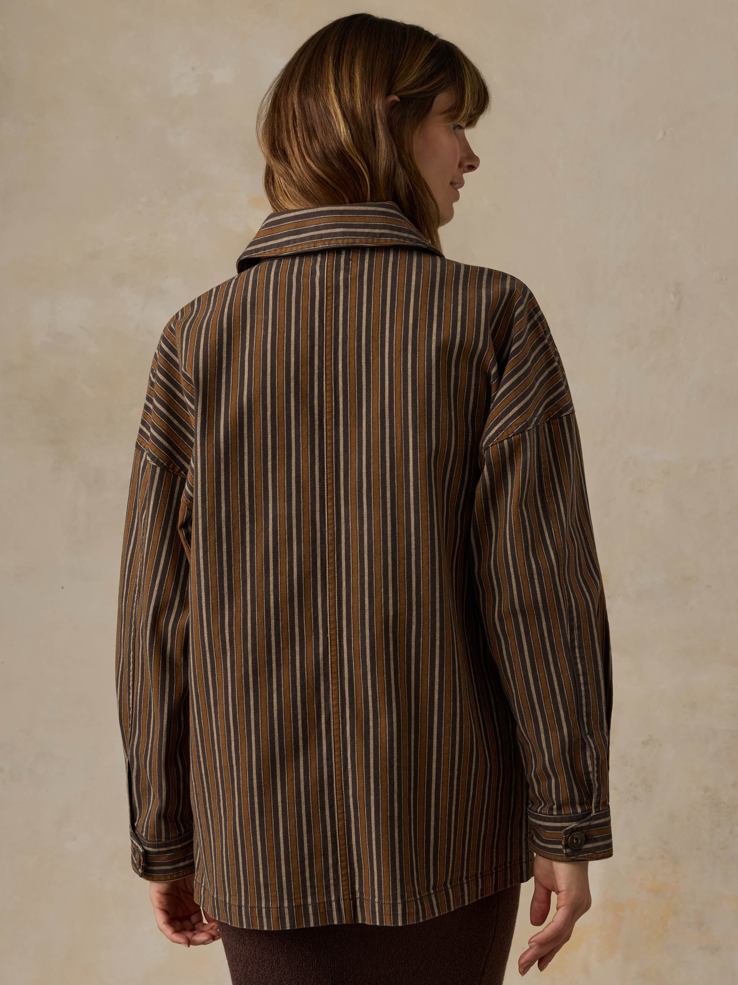 Woman wearing a brown striped chore jacket against a beige background