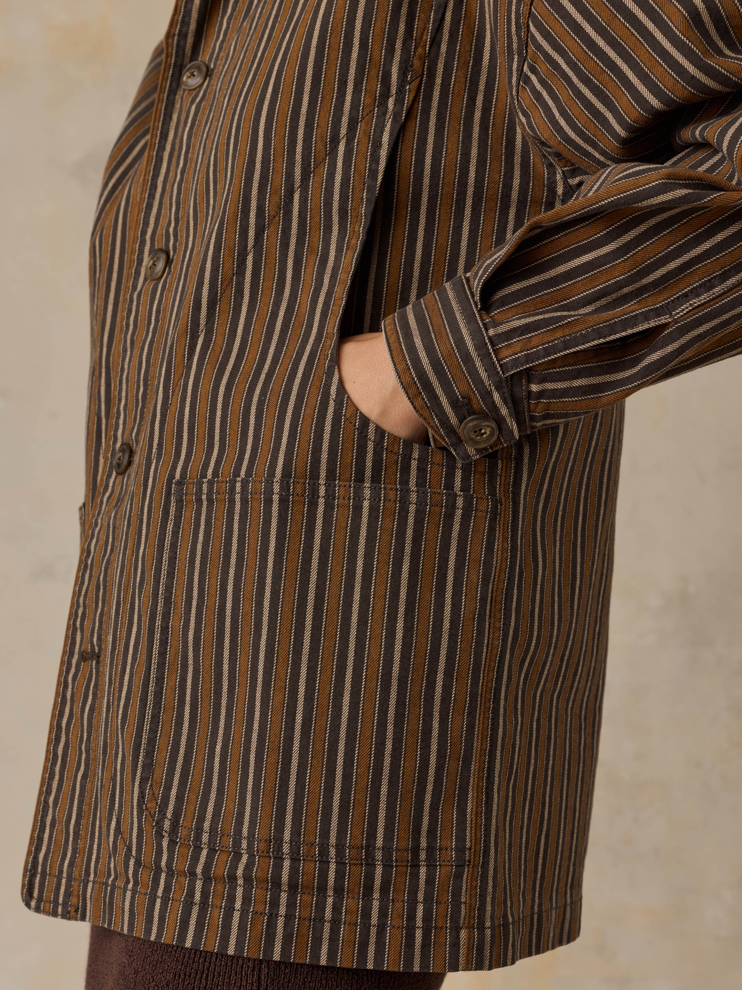 Woman wearing a brown striped chore jacket against a beige background