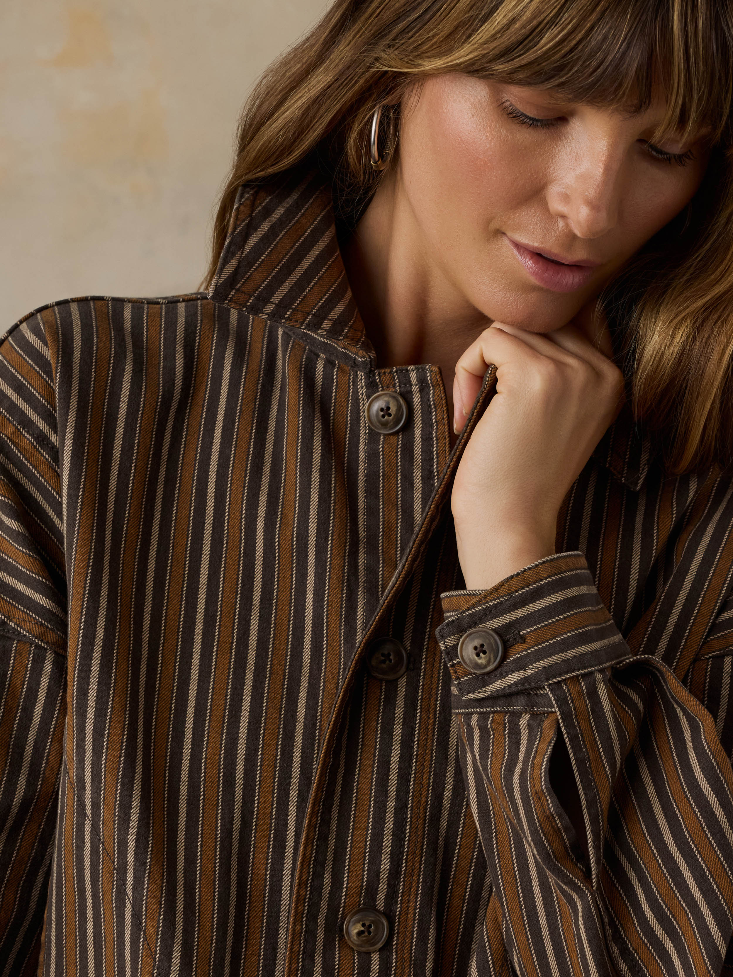Woman wearing a brown striped chore jacket against a beige background