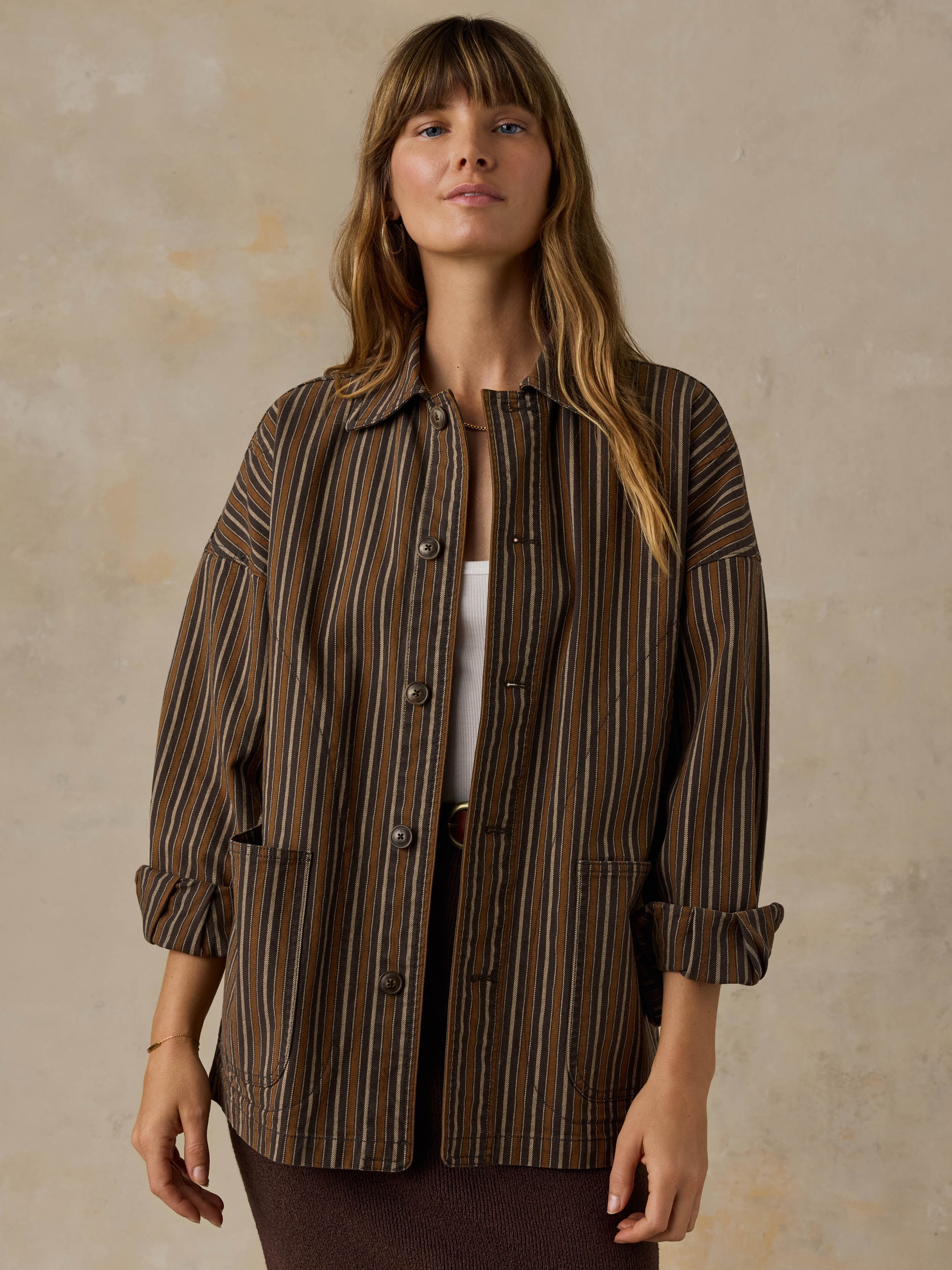 Woman wearing a brown striped chore jacket against a beige background