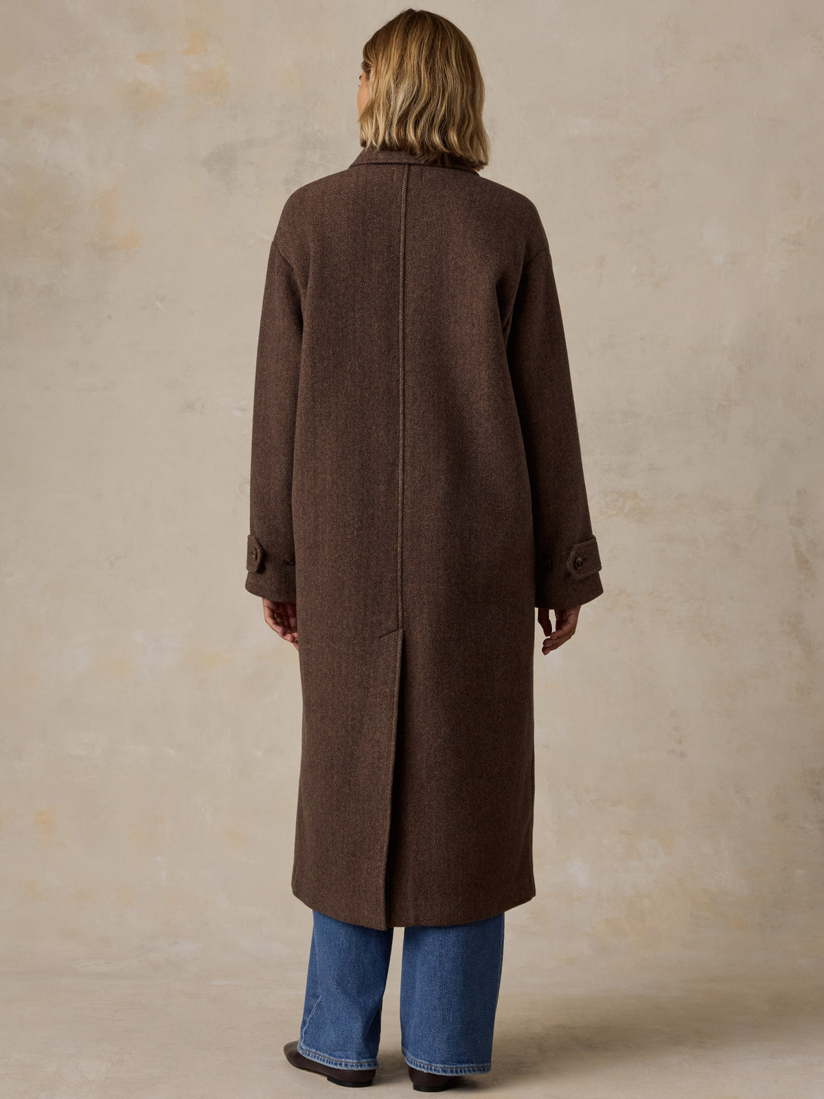 A woman viewed from the back wearing a brown long coat and blue jeans, image 4 of 9