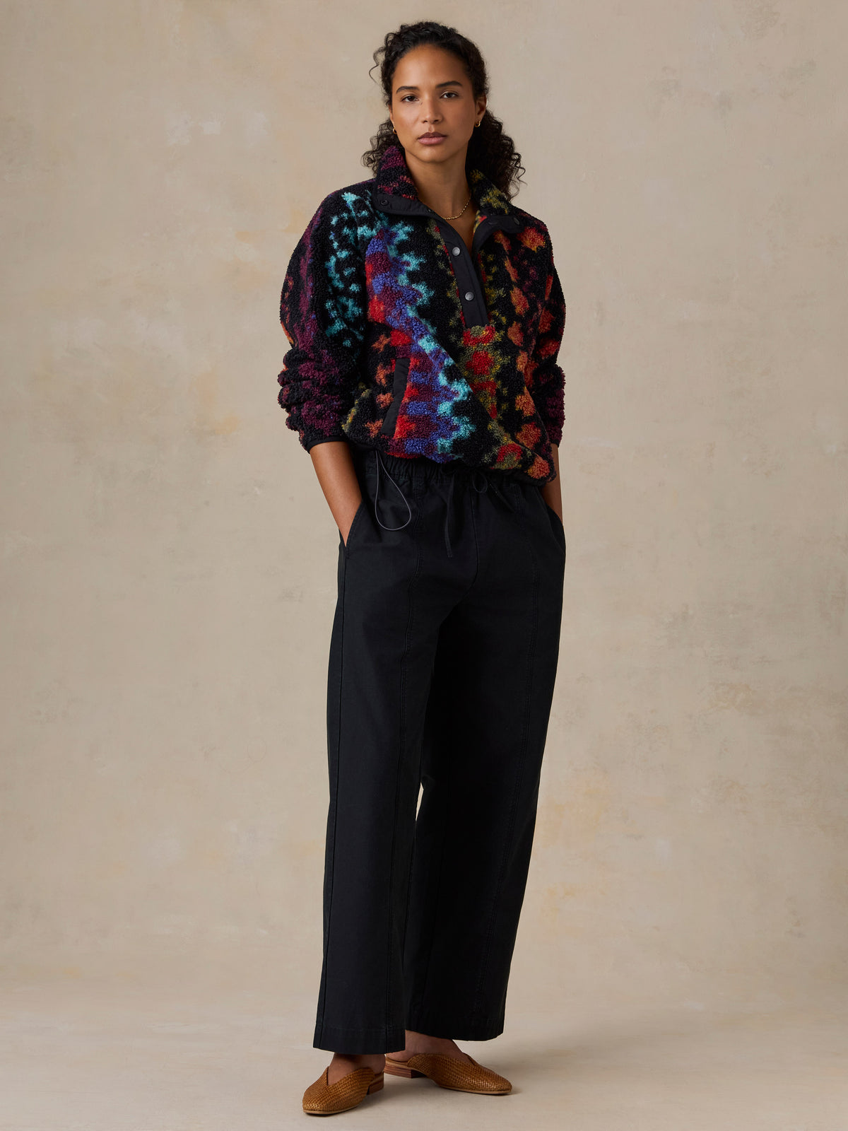 A woman wearing a colorful, patterned fleece pullover and black drawstring pants, image 4 of 7