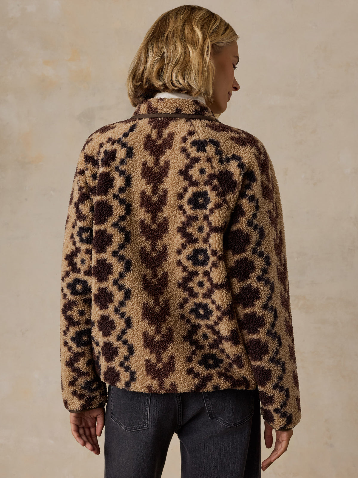 A woman viewed from behind wearing a brown printed fleece jacket and black jeans, image 3 of 5
