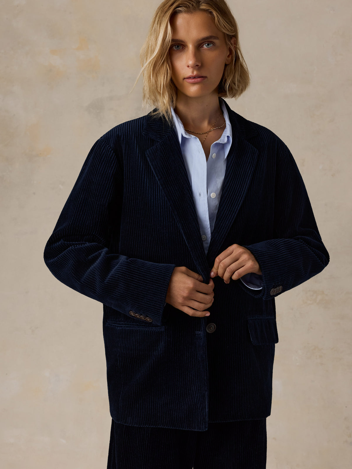 A woman wearing a dark navy corduroy suit with a light blue shirt, image 6 of 7
