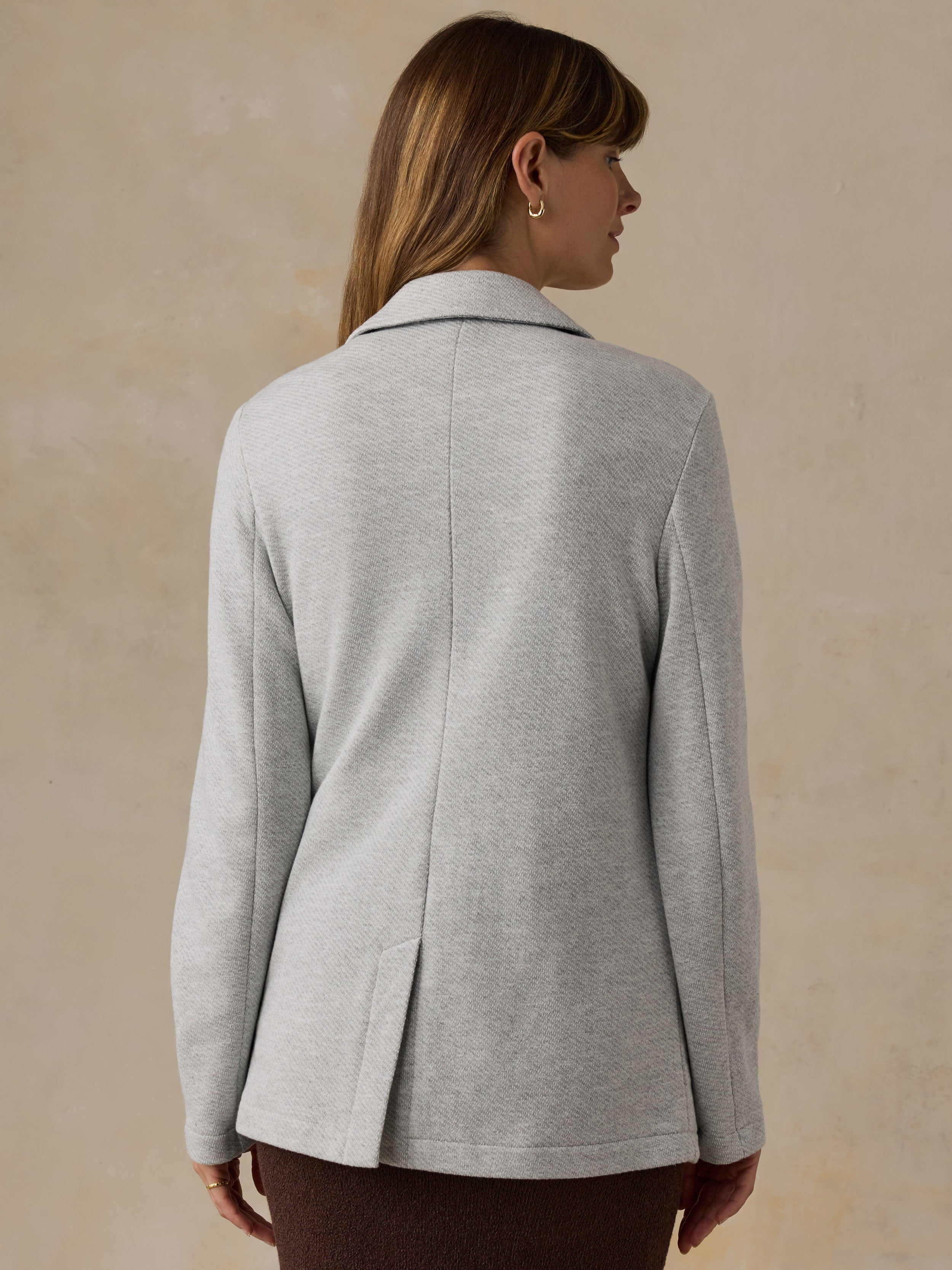 Woman wearing a grey blazer and brown skirt against a beige background