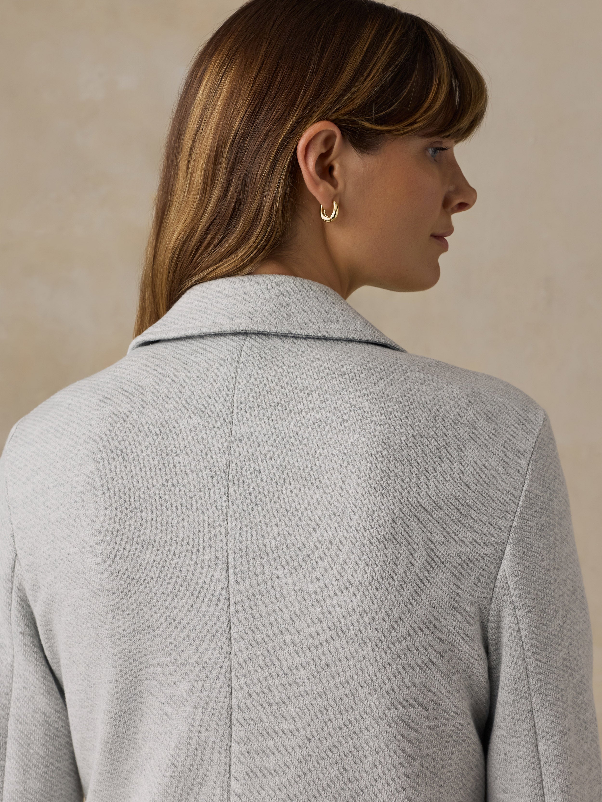 Woman wearing a grey blazer against a beige background