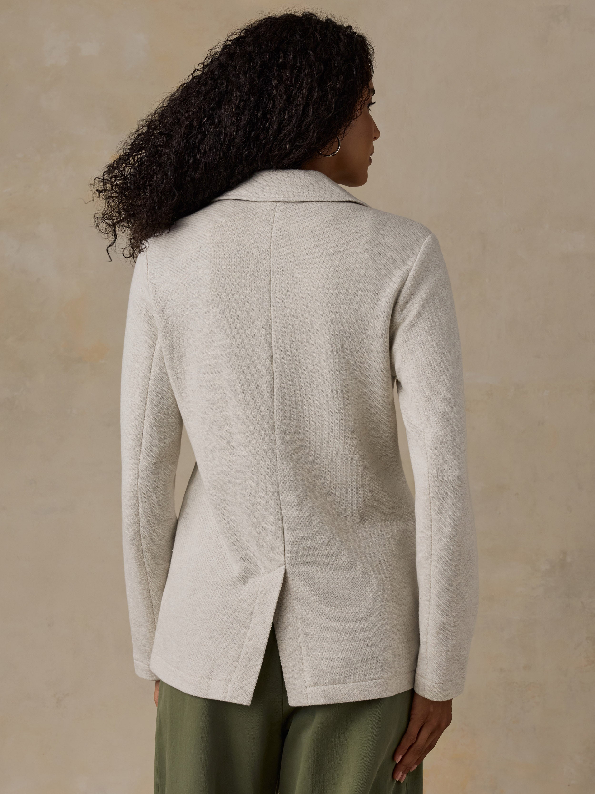 Woman wearing an oatmeal melange blazer and olive green pants against a beige background