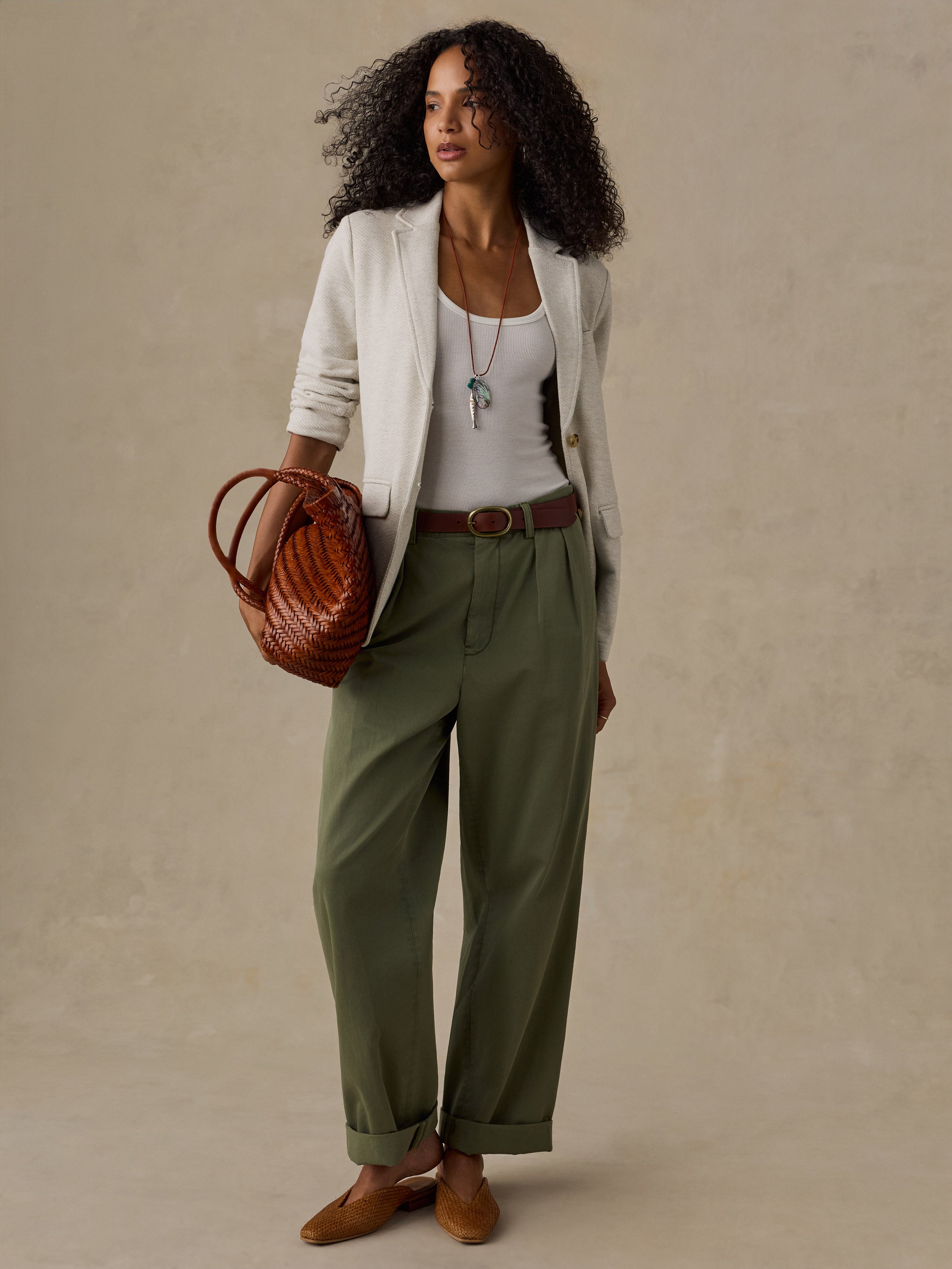 Woman wearing an oatmeal melange blazer over a white tank top and olive green pants against a beige background