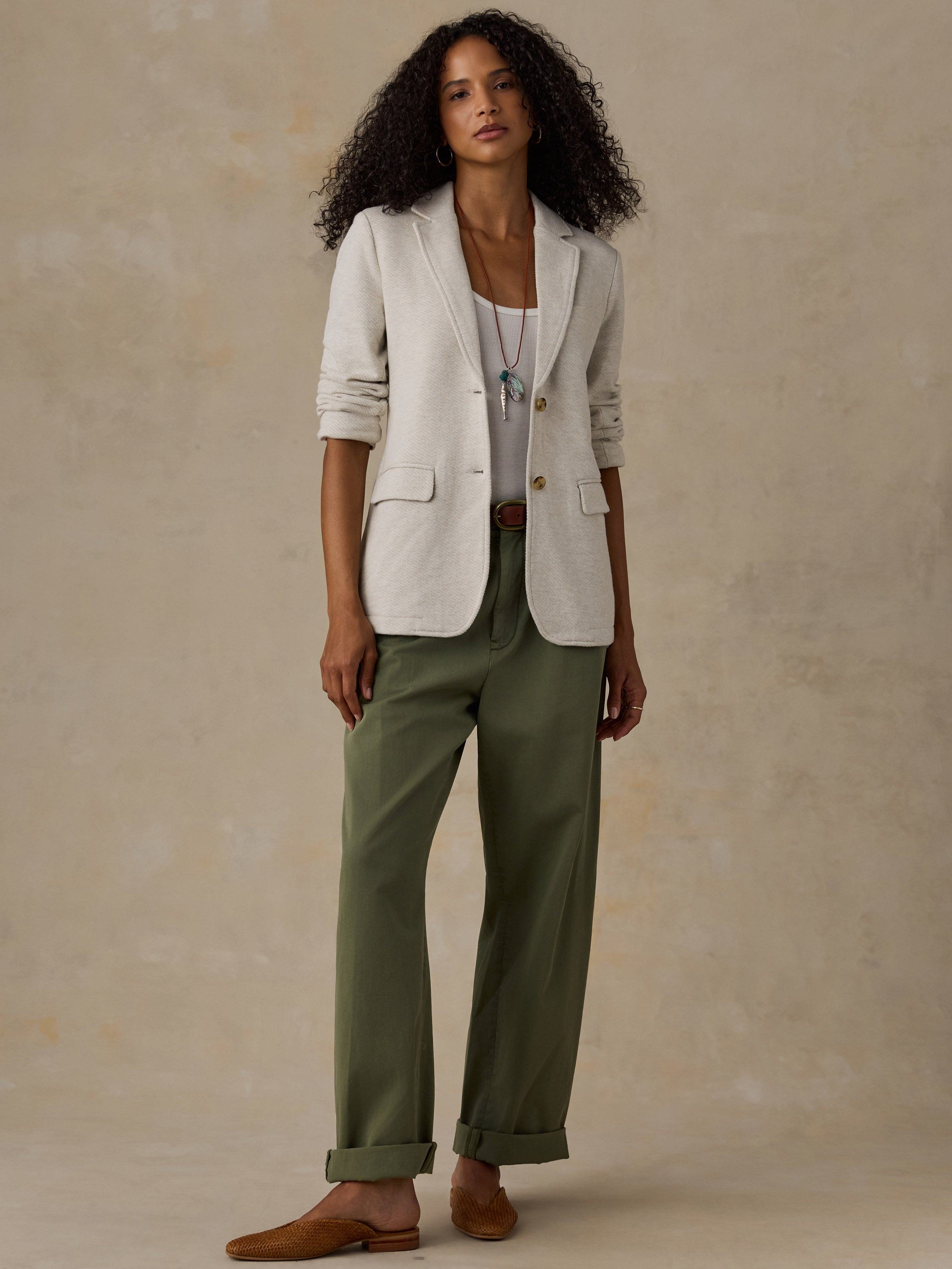 Woman wearing an oatmeal melange blazer over a white tank top and olive green pants against a beige background