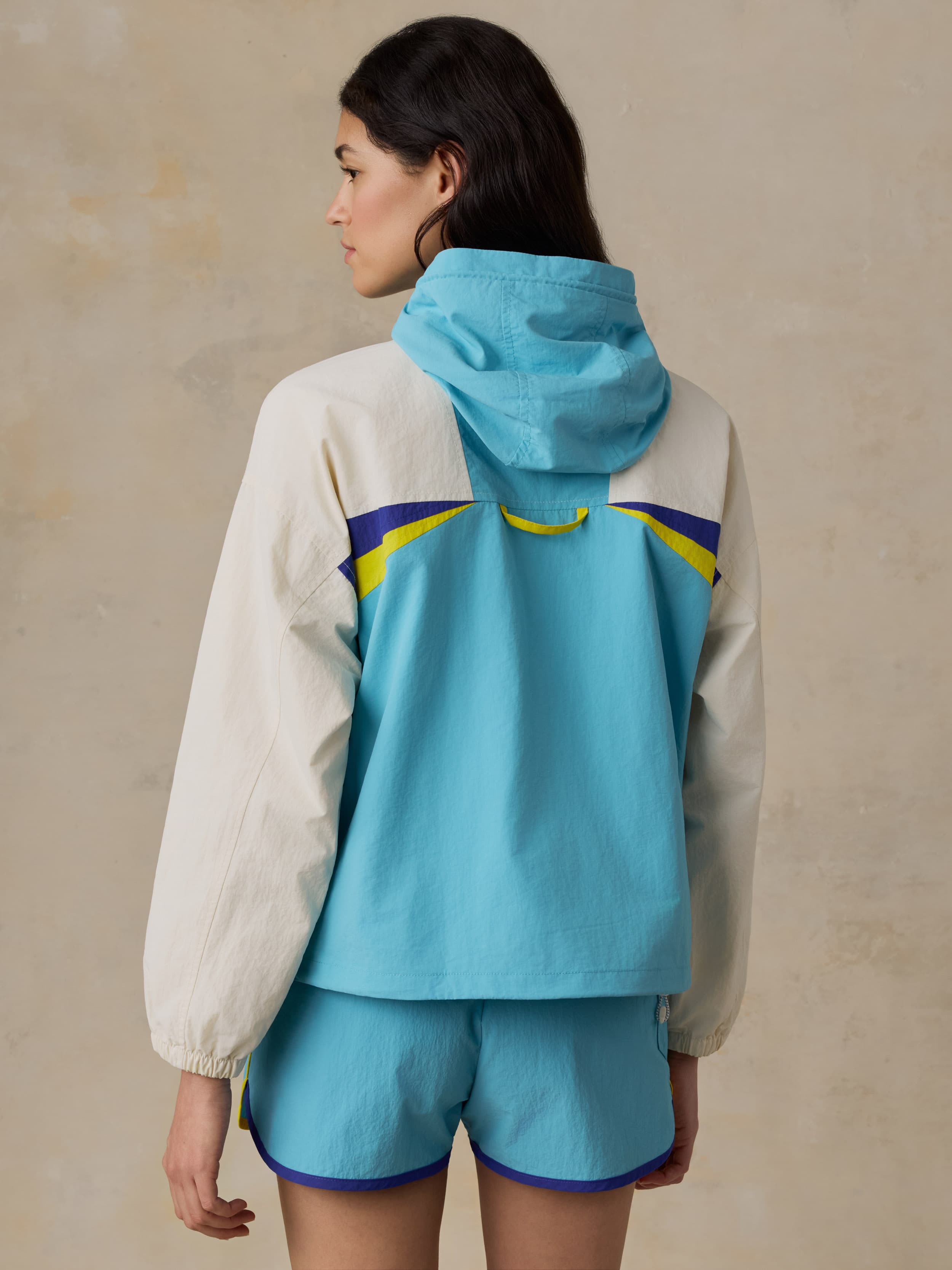 Woman wearing a colorful windbreaker jacket against a beige background