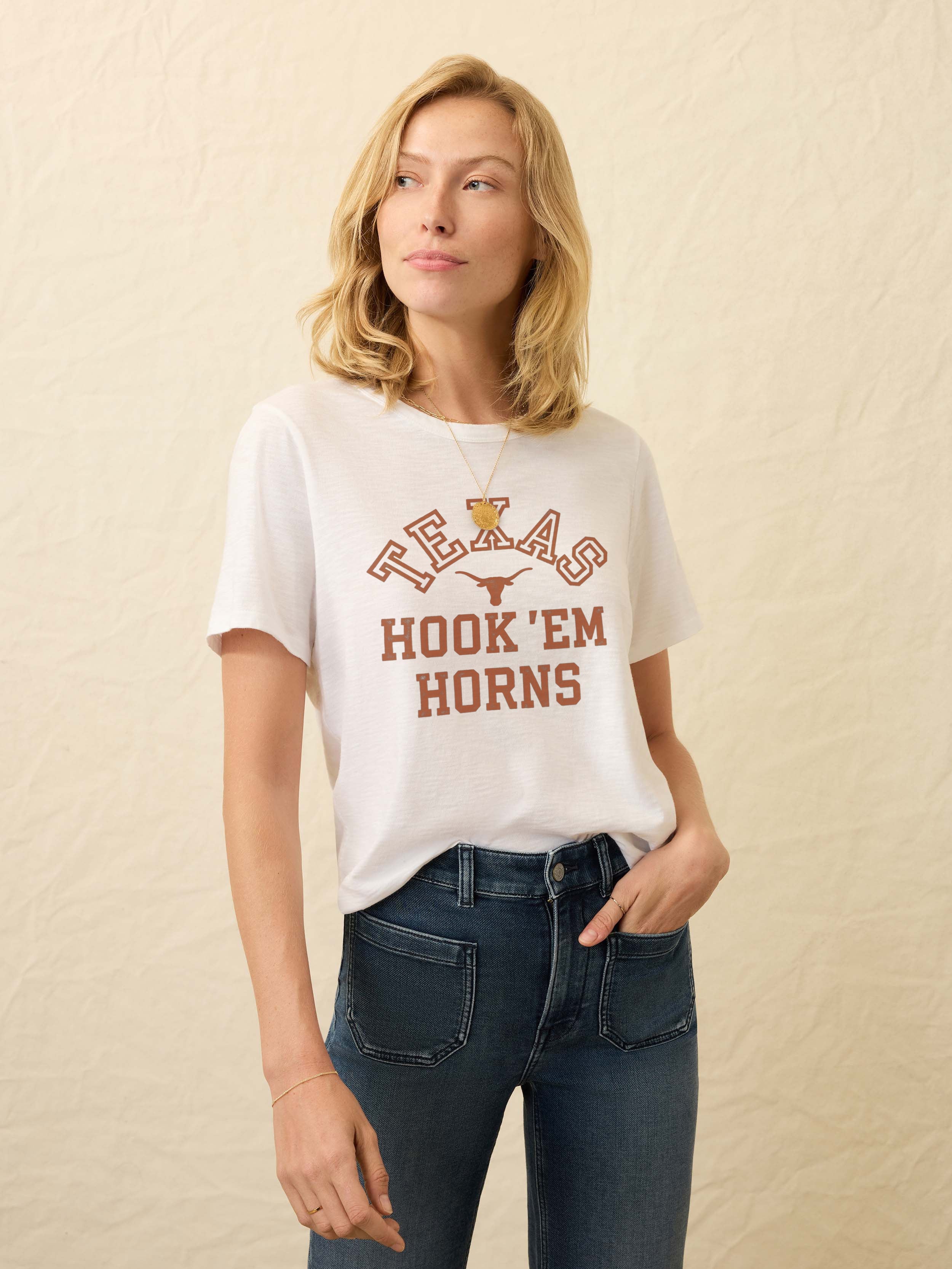 Woman wearing a white short sleeve t-shirt with UT Austin graphic on the center front against a beige background