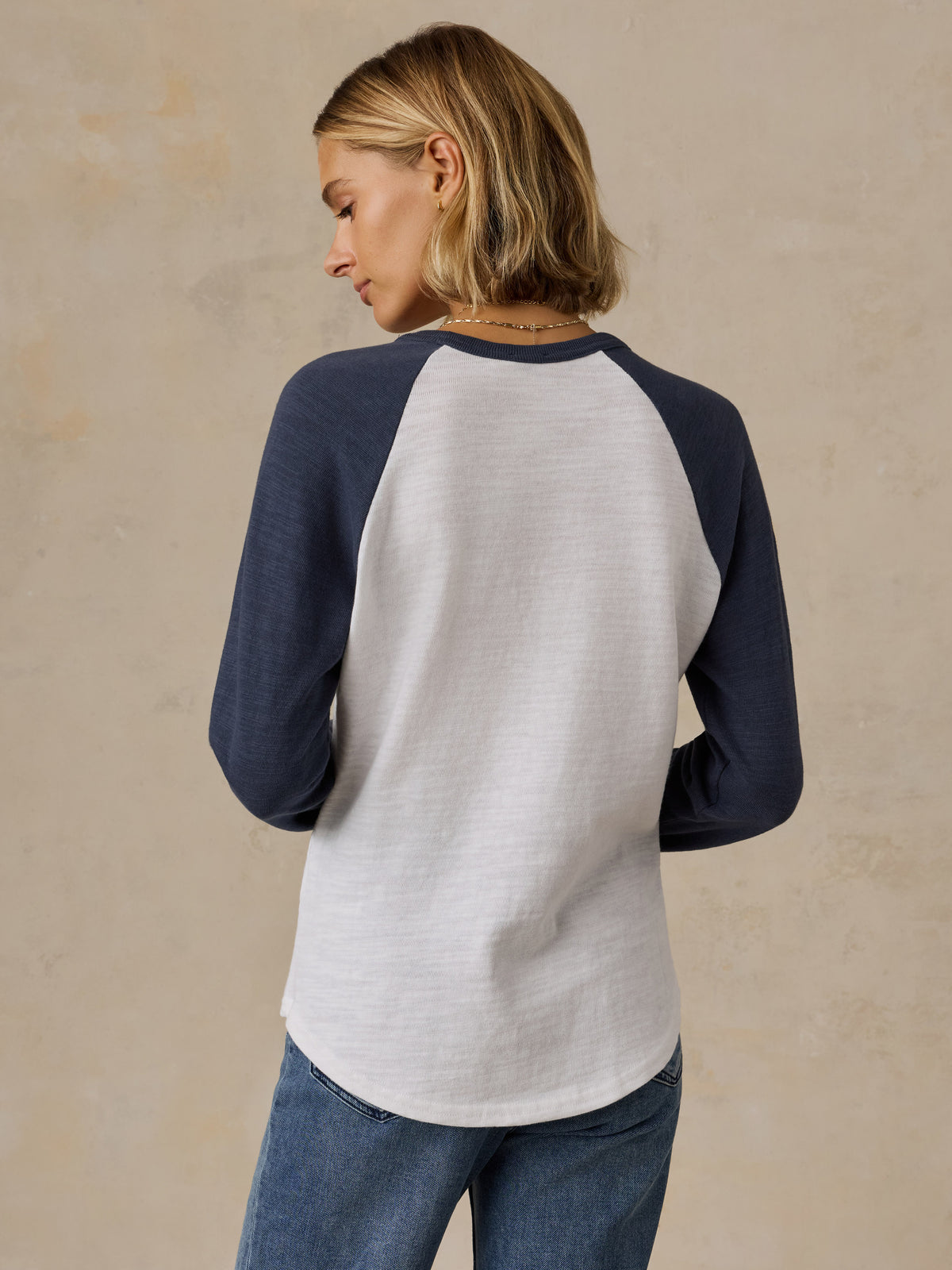 A woman viewed from behind wearing a blue and white NY Knicks baseball tee, image 5 of 6
