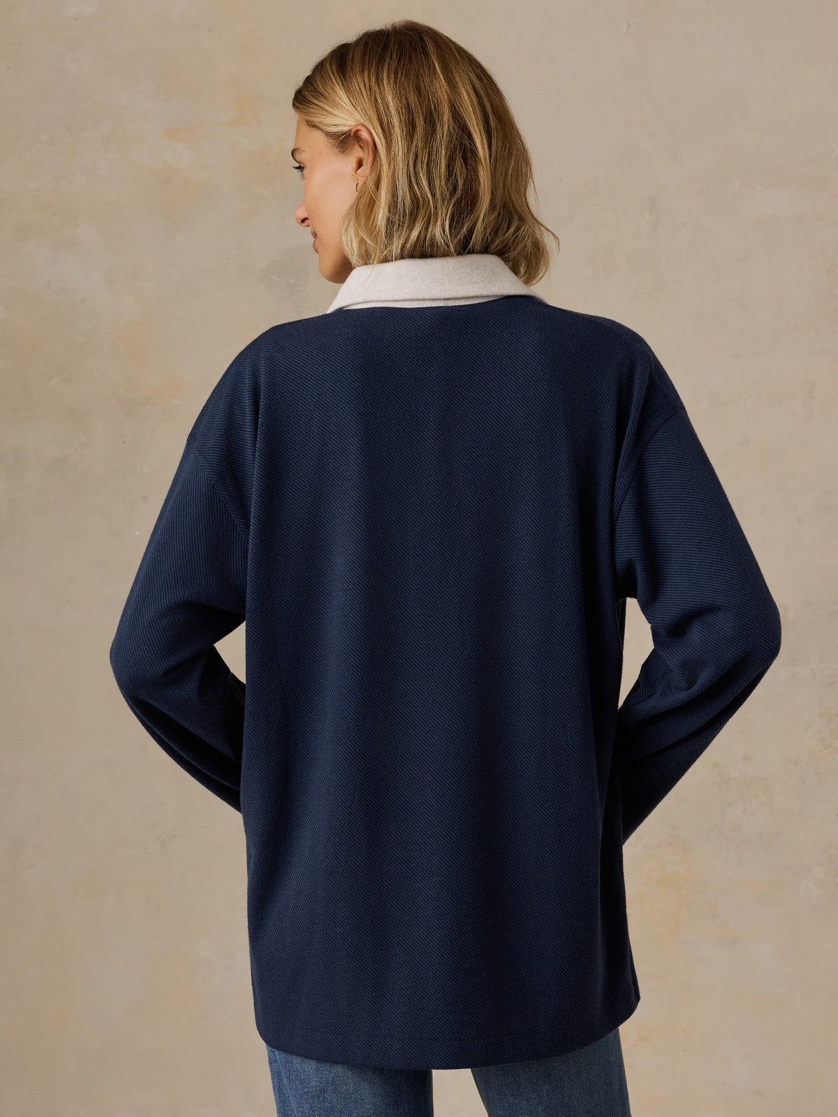 A woman viewed from behind wearing a navy NY Knicks rugby and blue jeans, image 2 of 6