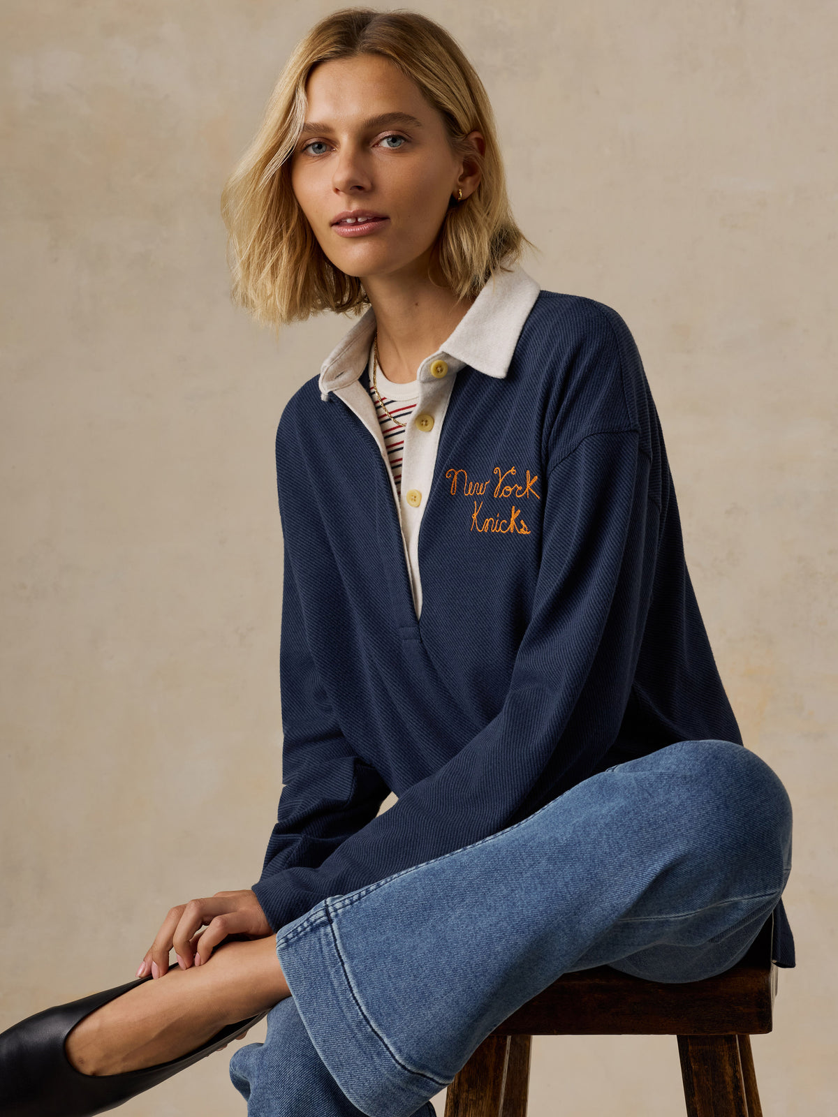 A woman wearing a navy NY Knicks rugby and blue jeans, image 4 of 6