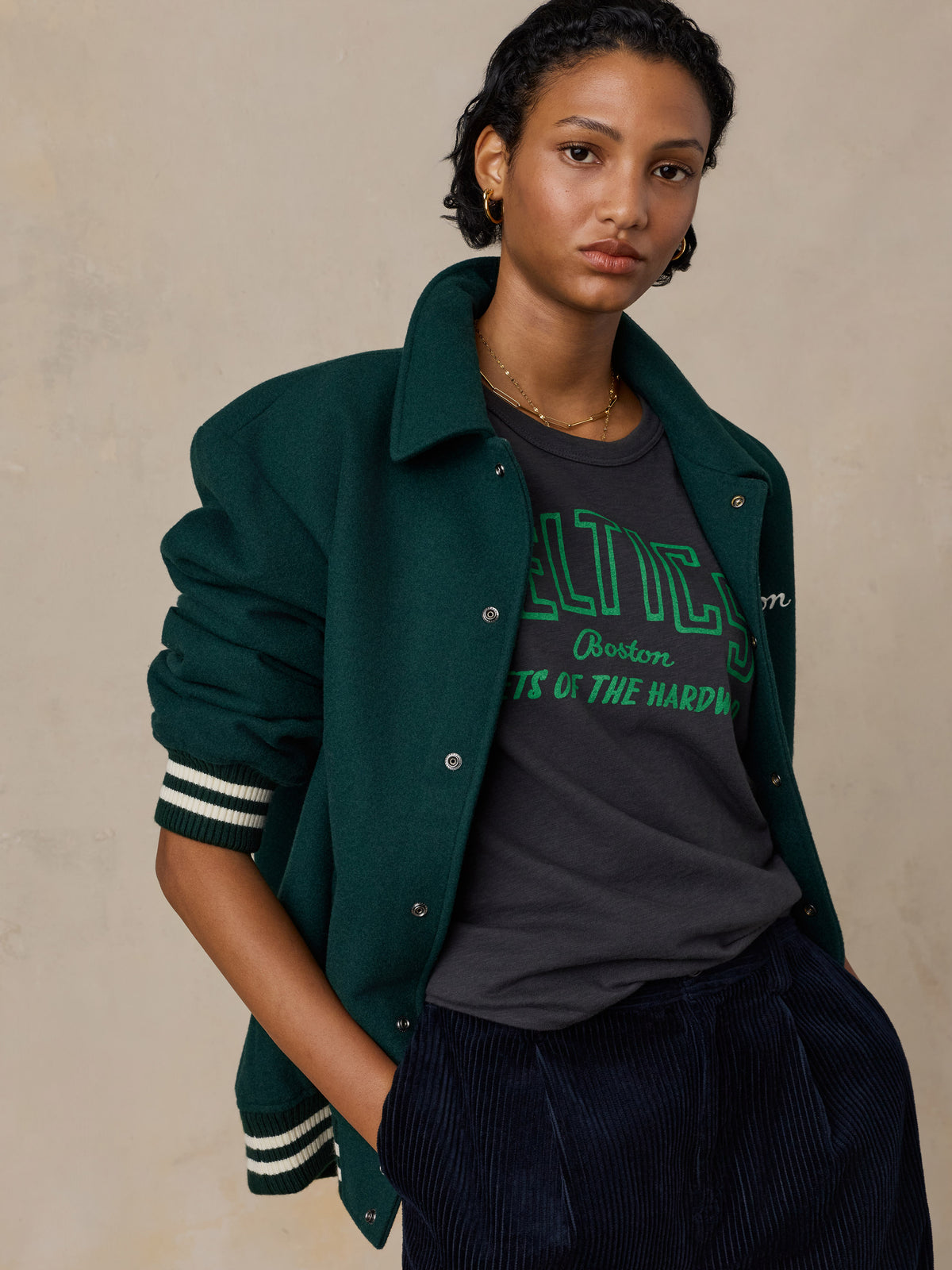 A woman wearing a black Boston Celtics tee and a varsity jacket, image 3 of 6