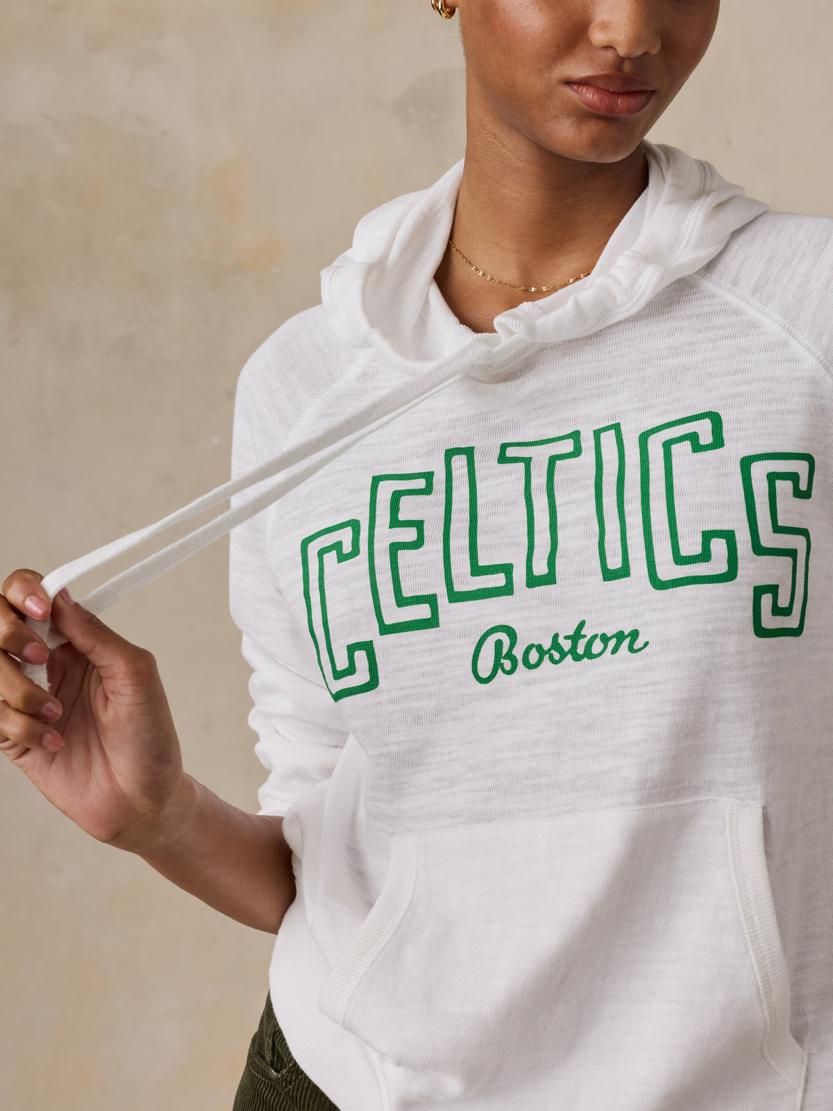 Close up of a woman wearing a white Boston Celtics hoodie and green pants, image 3 of 5