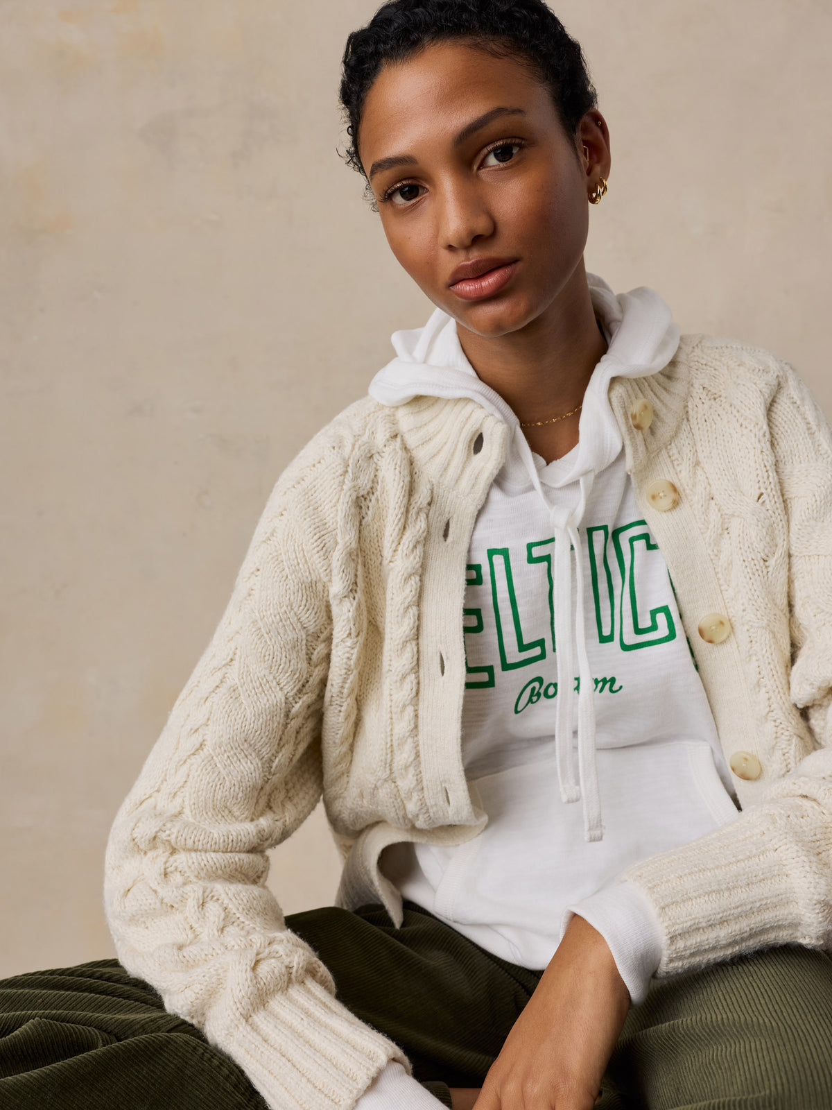A woman wearing a white Boston Celtics hoodie and green pants, image 5 of 5