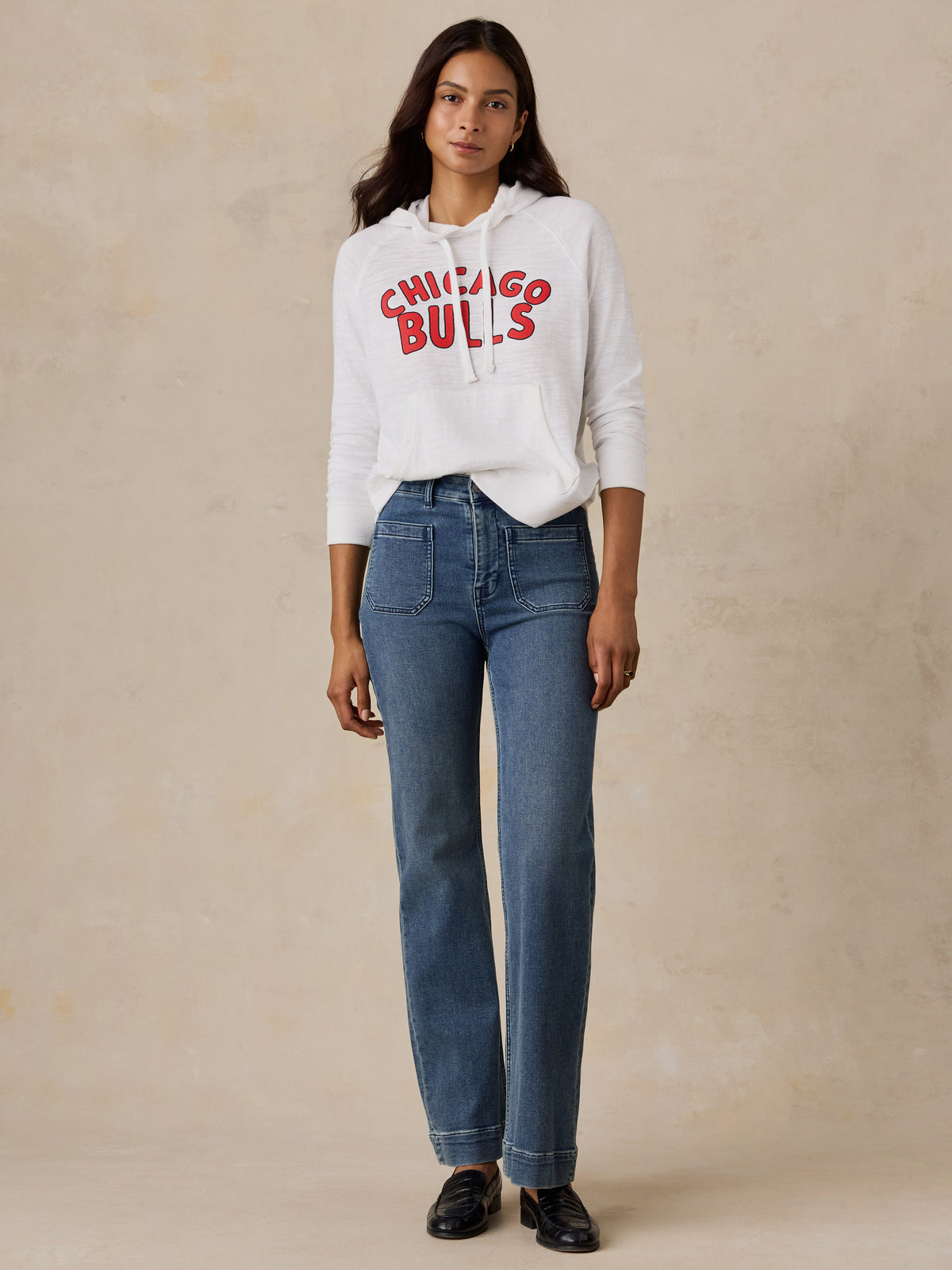 A woman wearing a white Chicago Bulls hoodie and blue jeans, image 5 of 5