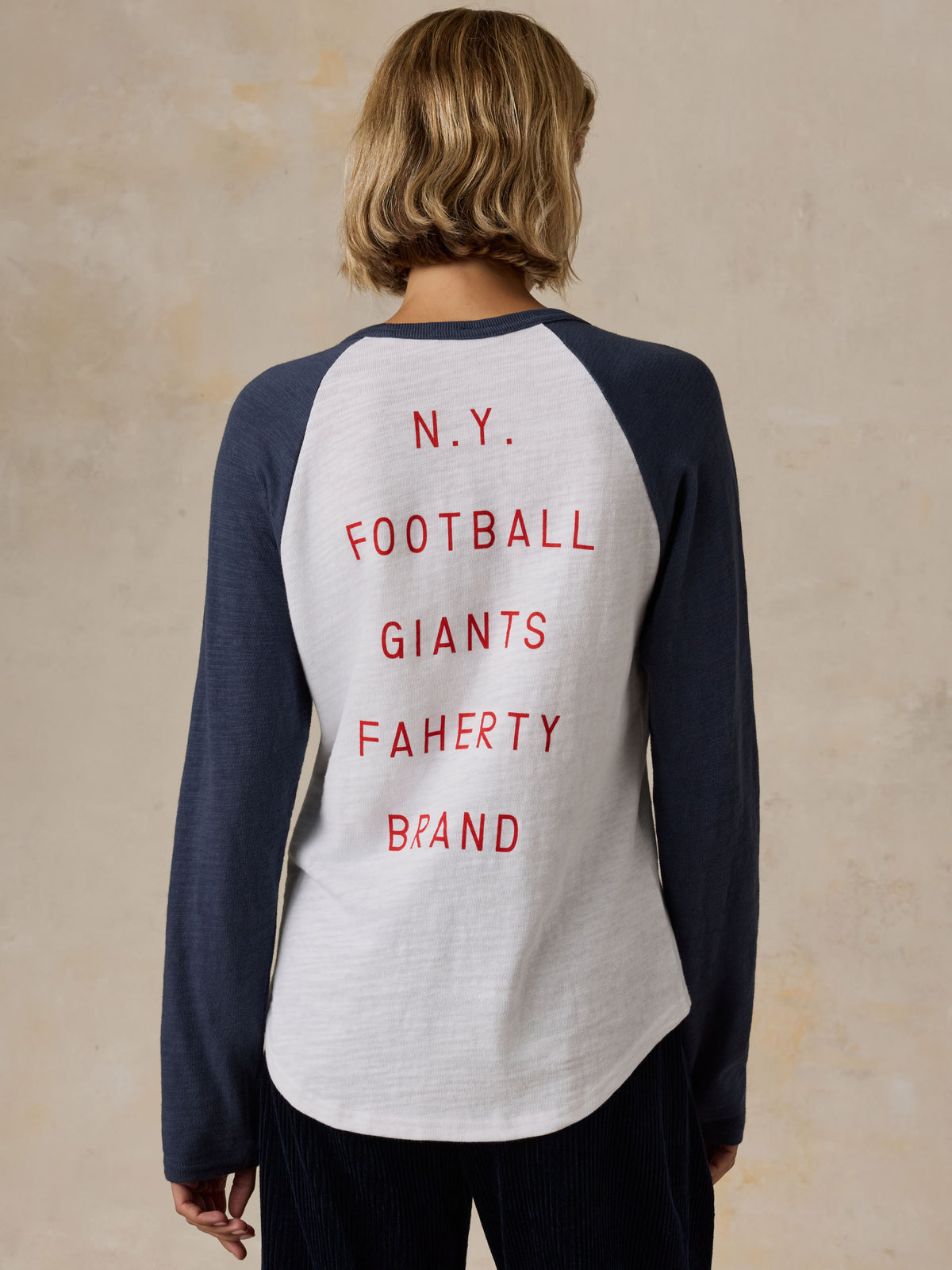 A woman viewed from the back wearing a white and blue NY Giants baseball tee with navy pants, image 3 of 5