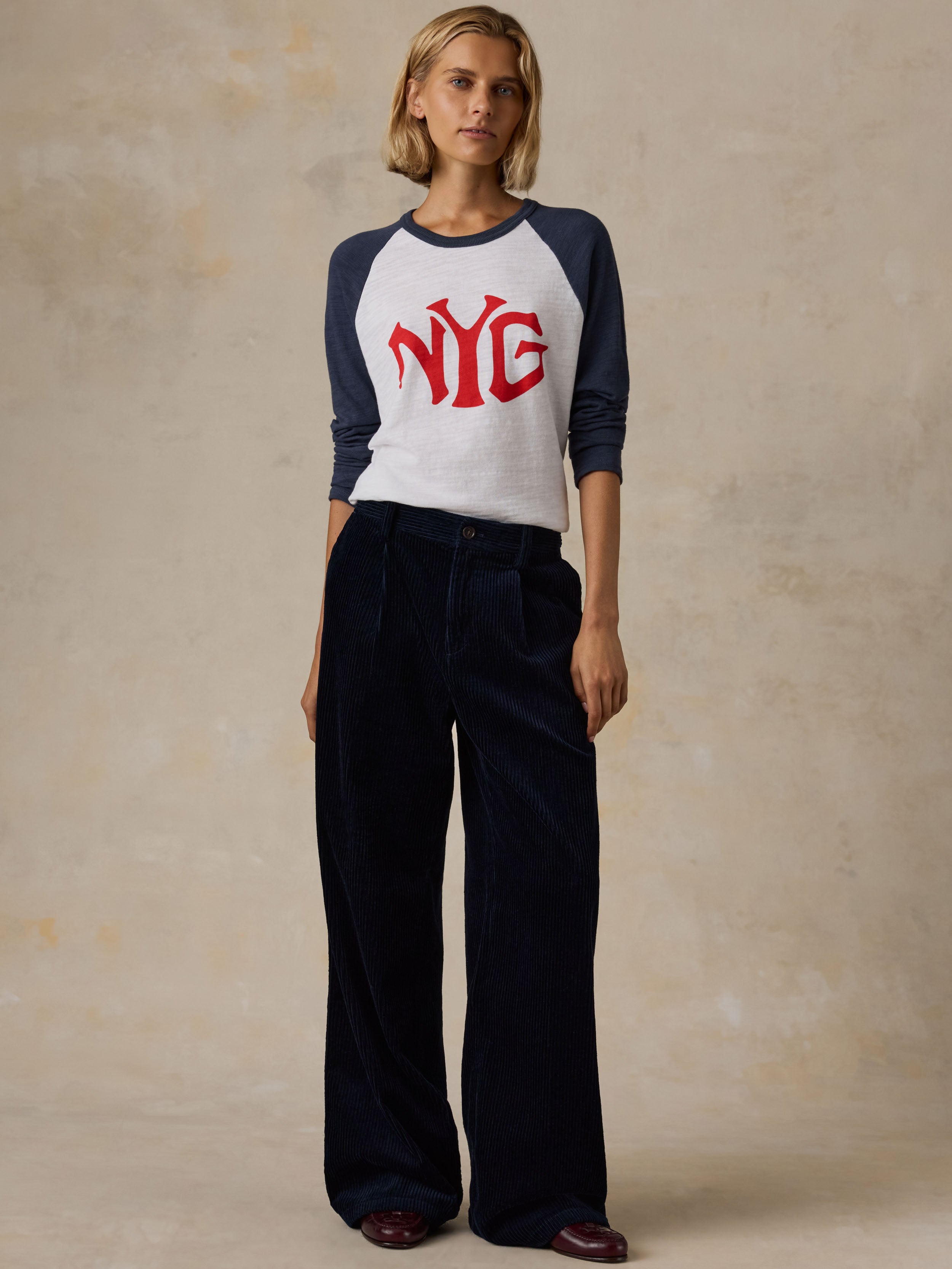 A woman wearing a white and blue NY Giants baseball tee with navy pants
