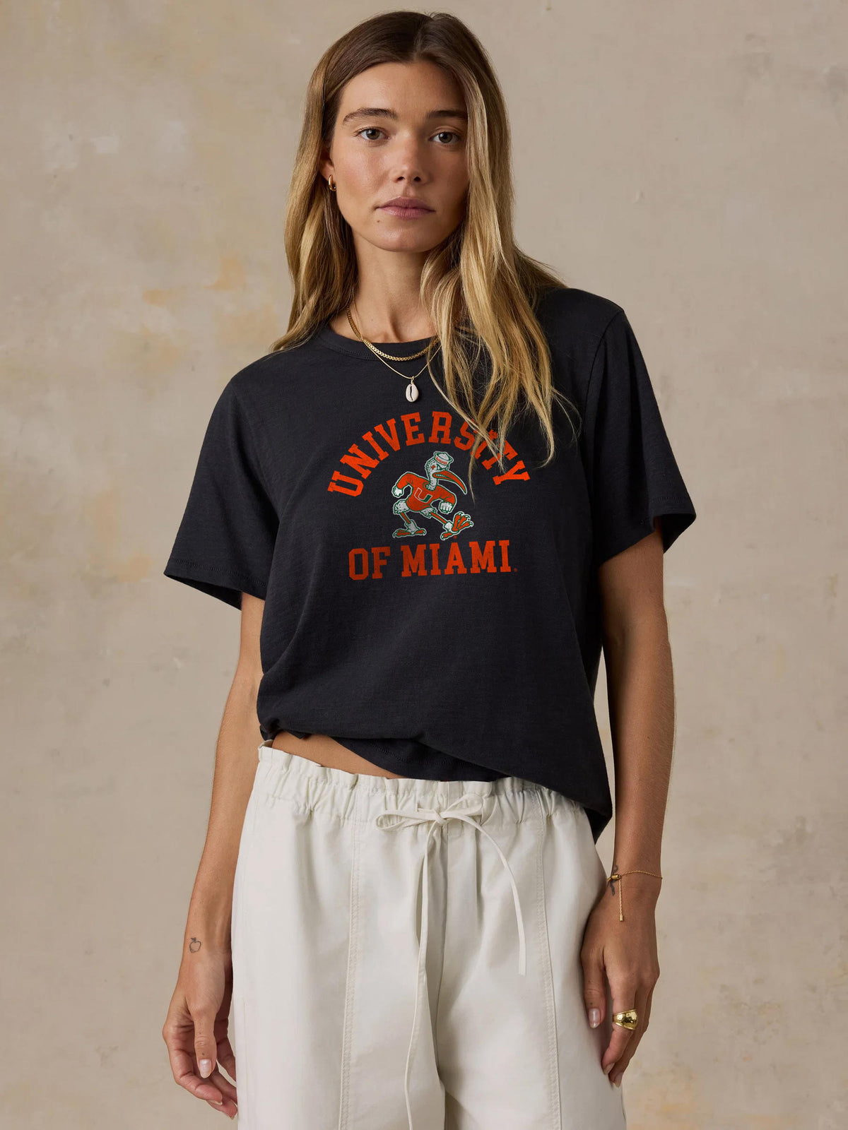 A woman wearing a black University of Miami tee and white pants, image 1 of 1