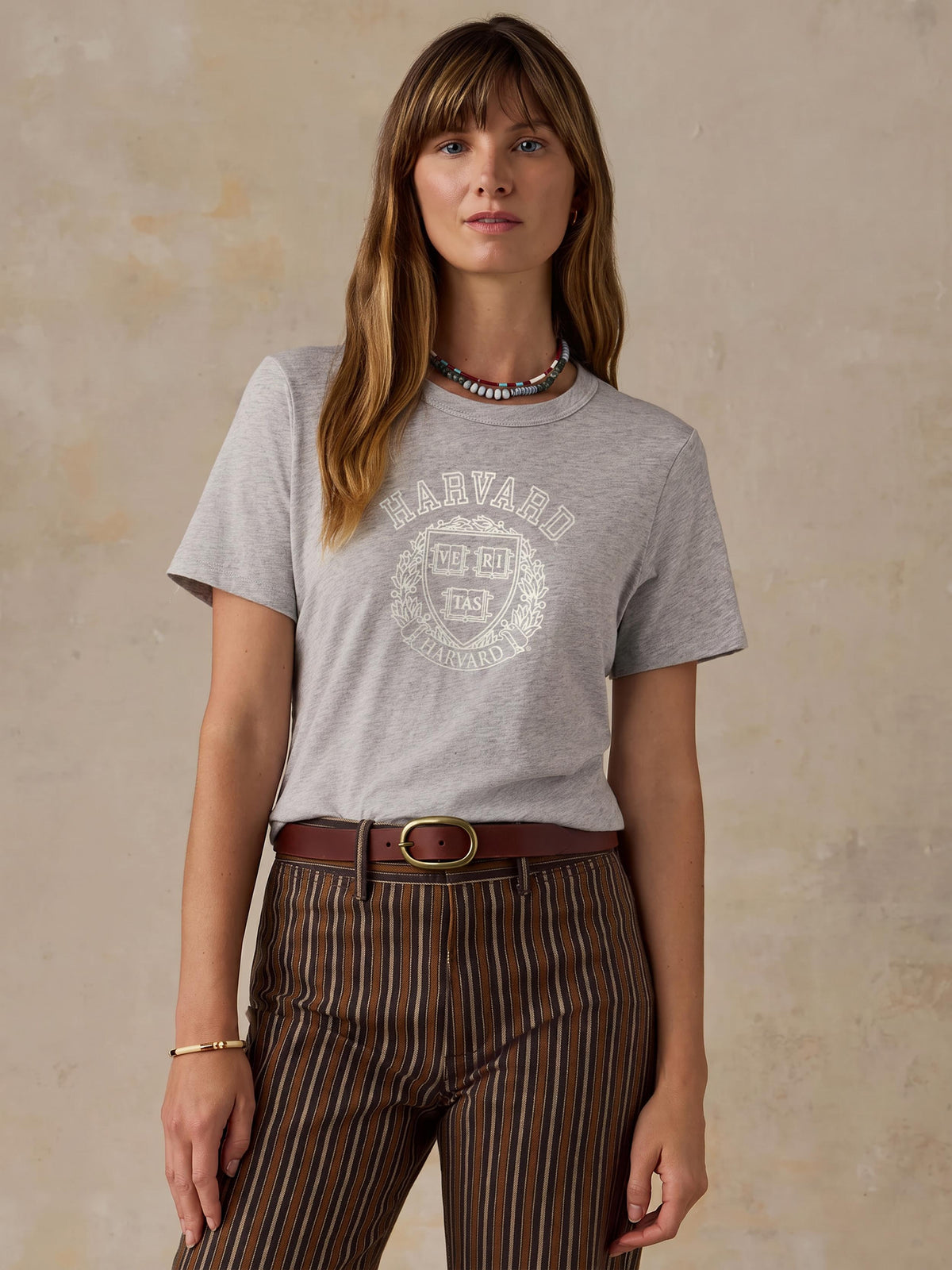 A woman wearing a grey harvard tee and brown striped pants, image 1 of 1