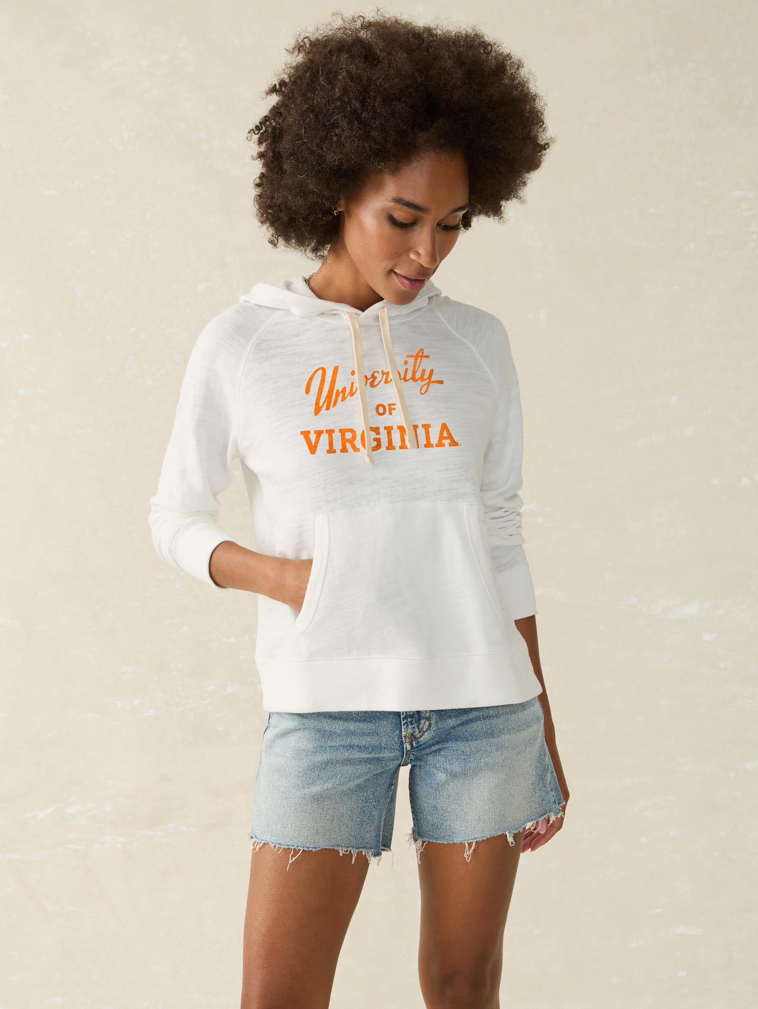 A woman wearing a white University of Virginia hoodie and denim shorts