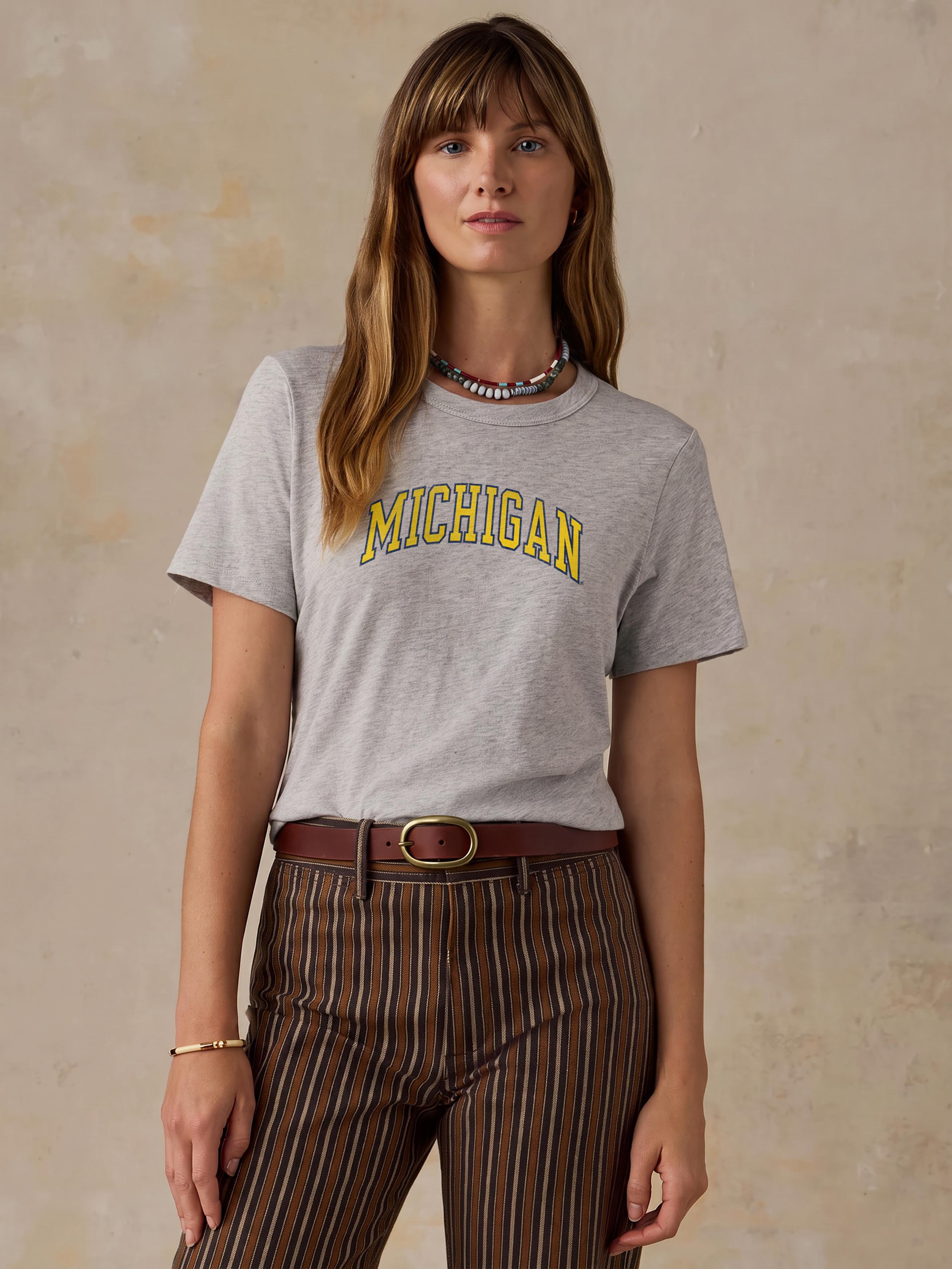 A woman wearing a grey University of Michigan tee and brown striped pants