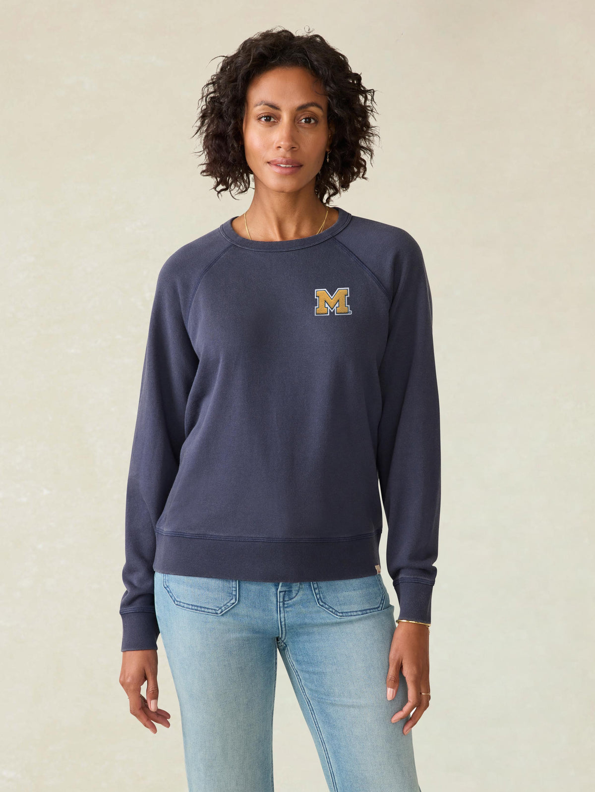 A woman wearing a blue University of Michigan crewneck and blue jeans, image 1 of 1