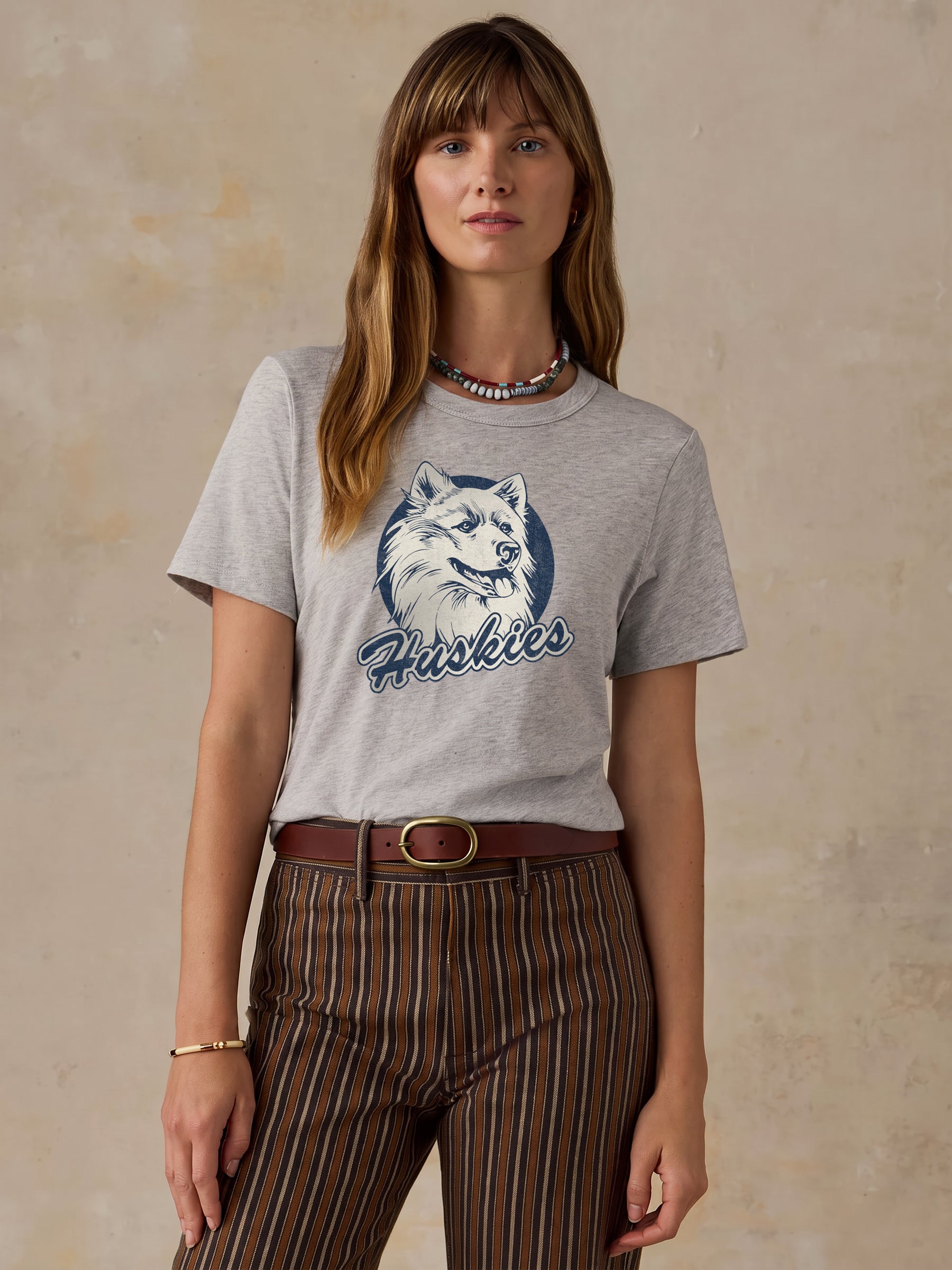 A woman wearing a grey UCONN tee and brown striped shorts