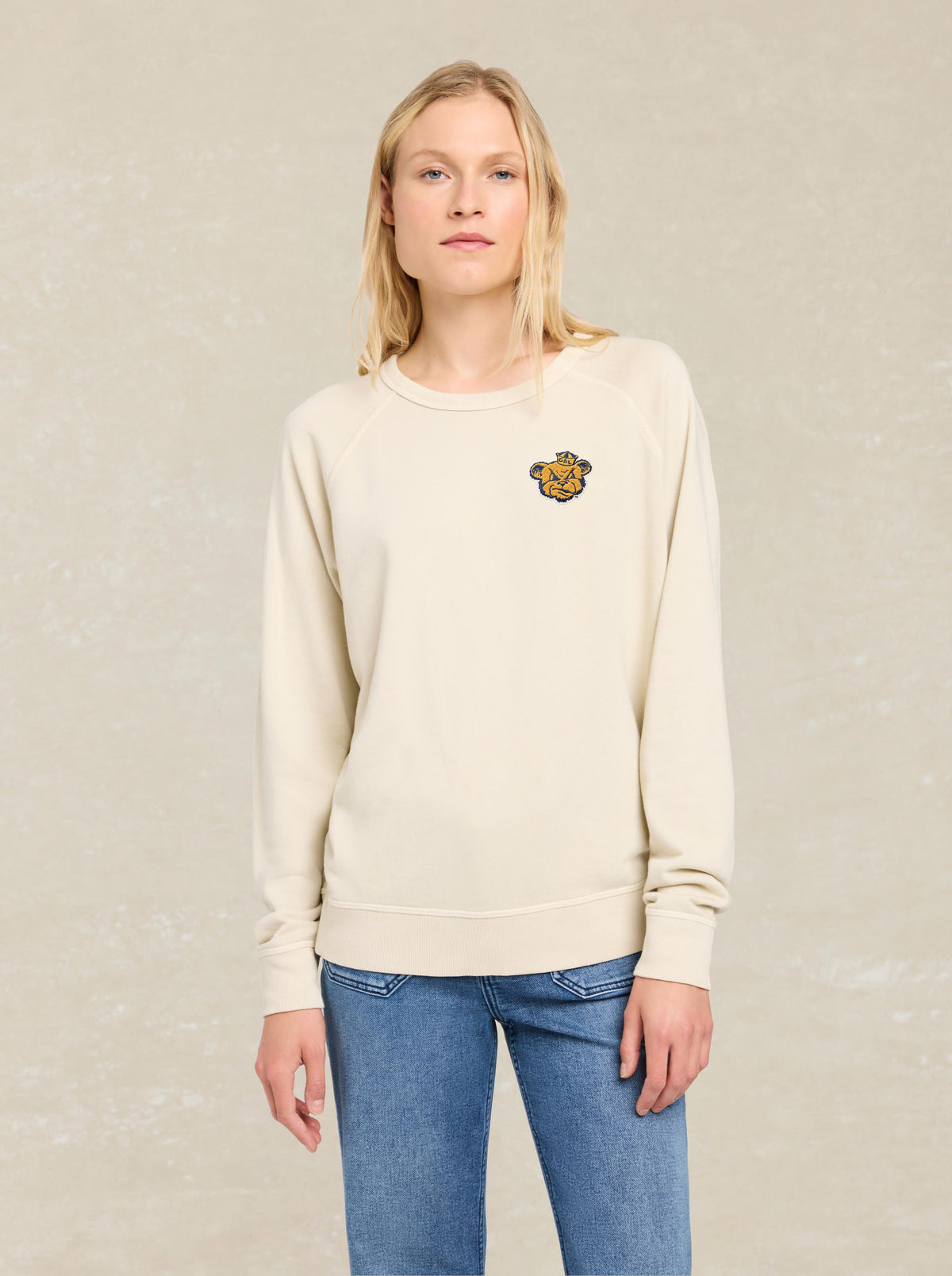 A woman wearing a white UC Berkeley crewneck and blue jeans, image 1 of 1