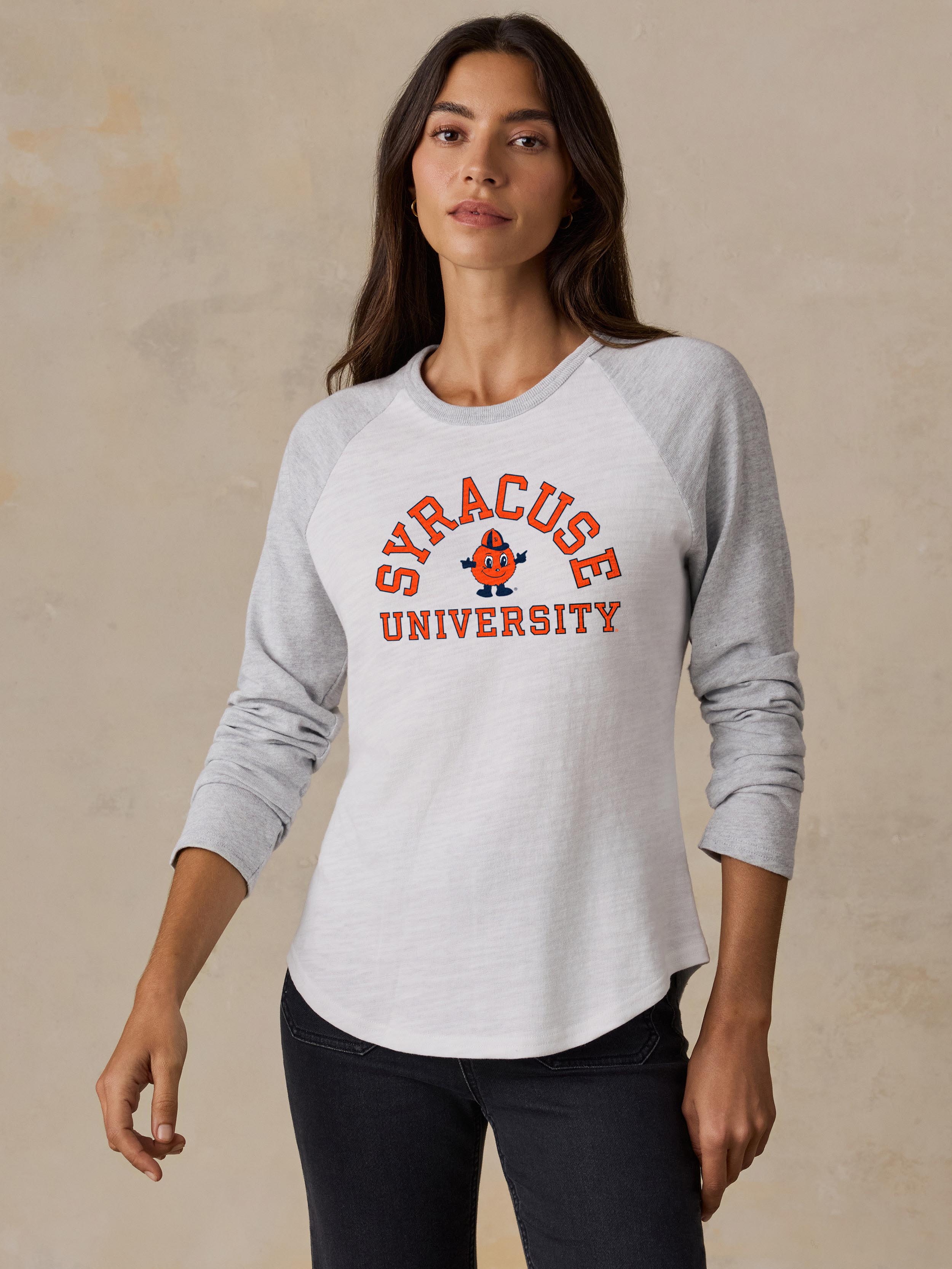 A woman wearing a white and grey Syracuse baseball tee and black jeans