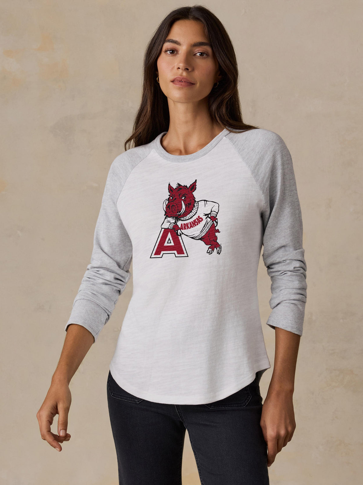 A woman wearing a white and grey Arkansas baseball tee and black jeans, image 1 of 2