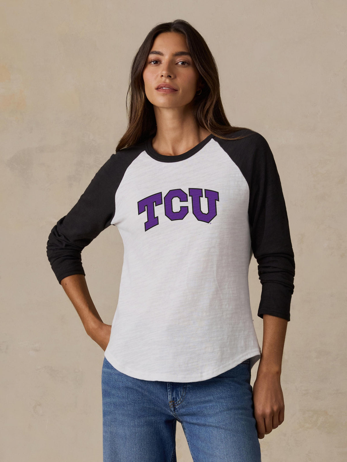 A woman wearing a black and white TCU baseball tee and blue jeans, image 1 of 2