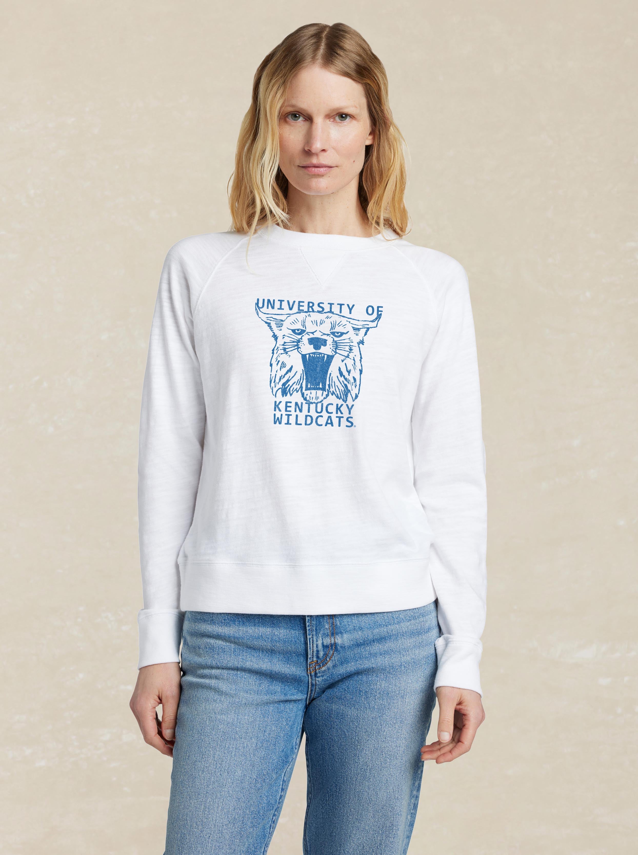 A woman wearing a white University of Kentucky crewneck and blue jeans