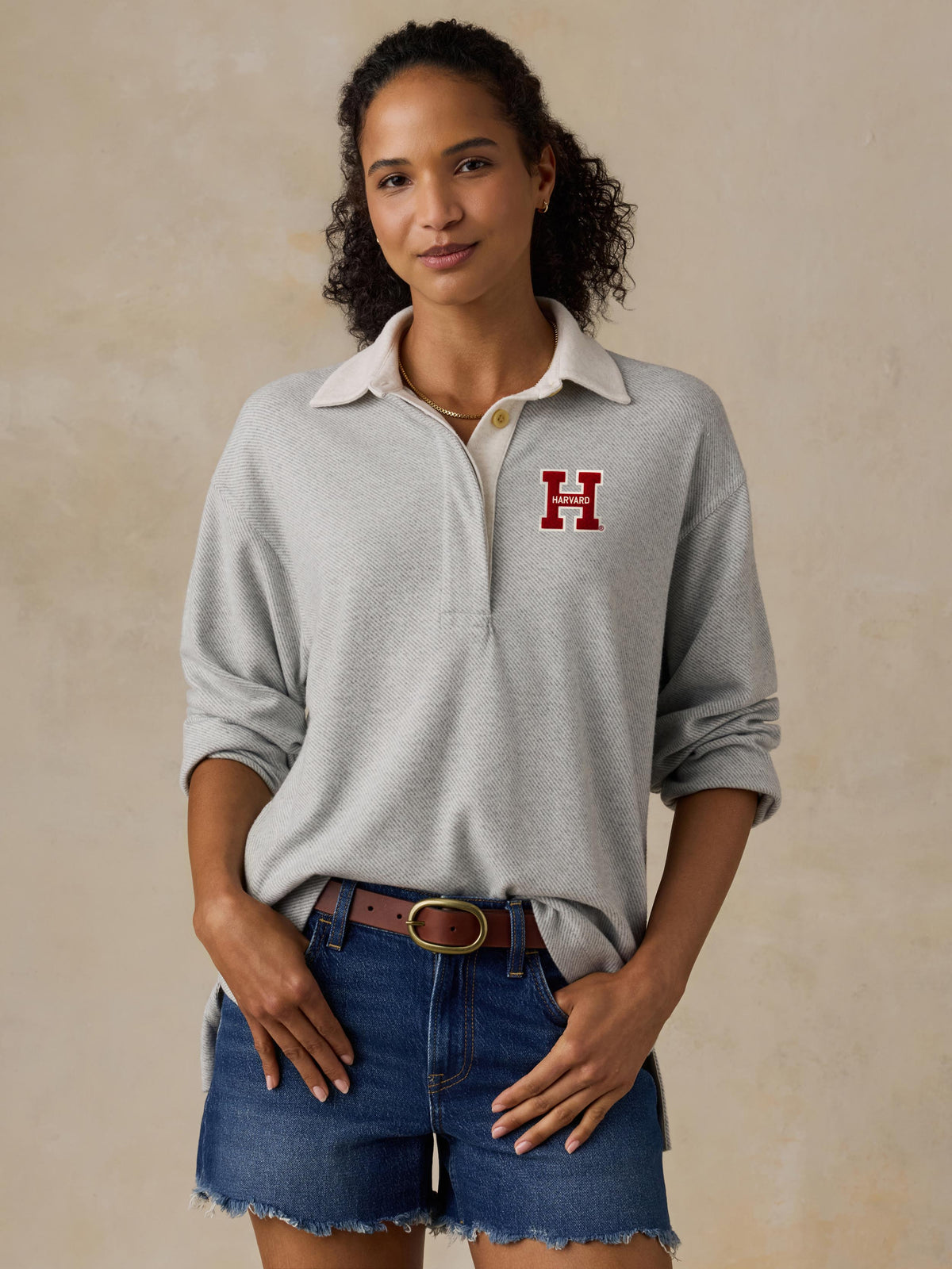 A woman wearing a grey Harvard rugby polo and denim shorts, image 1 of 1