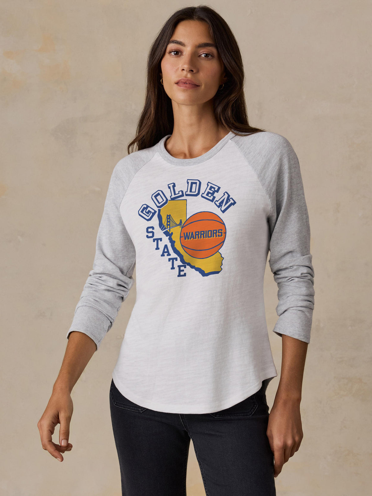 A woman wearing a white and grey Golden State Warriors baseball tee, image 1 of 2