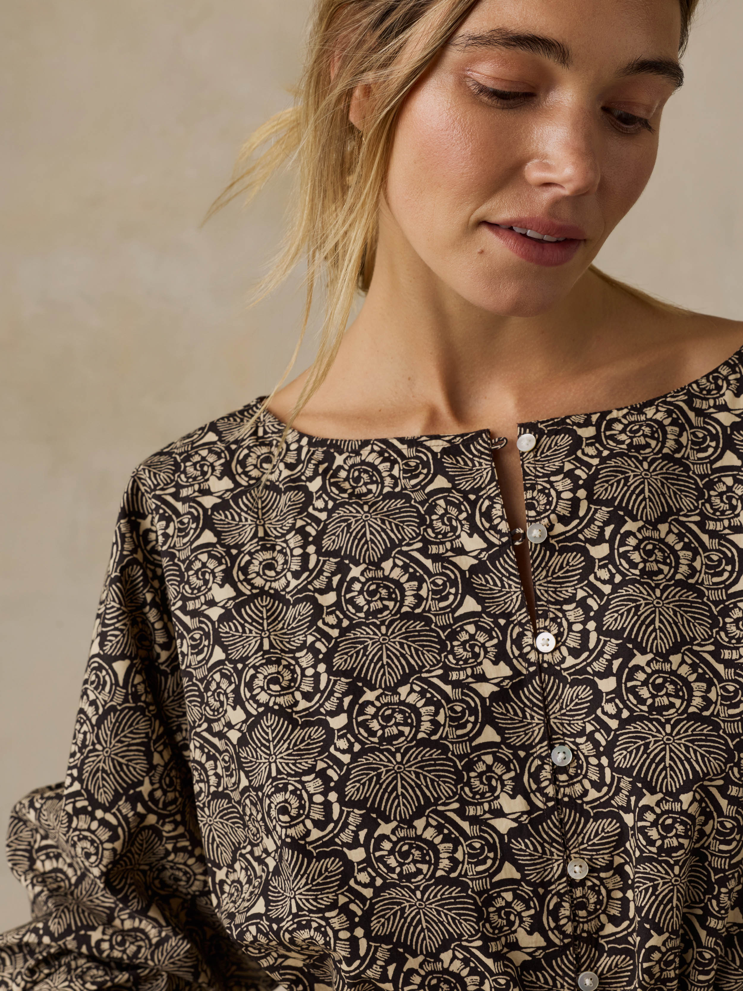 Woman wearing a black patterned blouse against a beige background