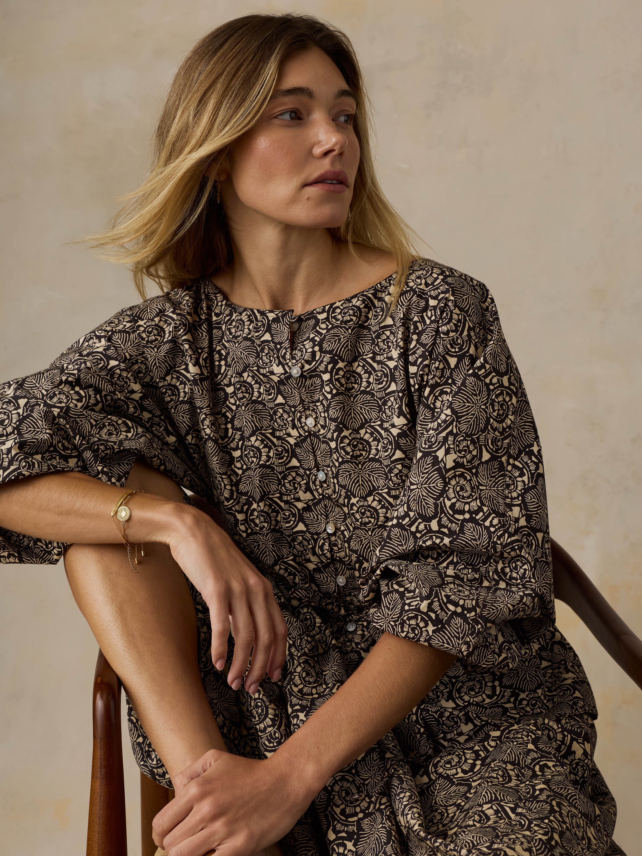 Woman wearing a black patterned blouse against a beige background