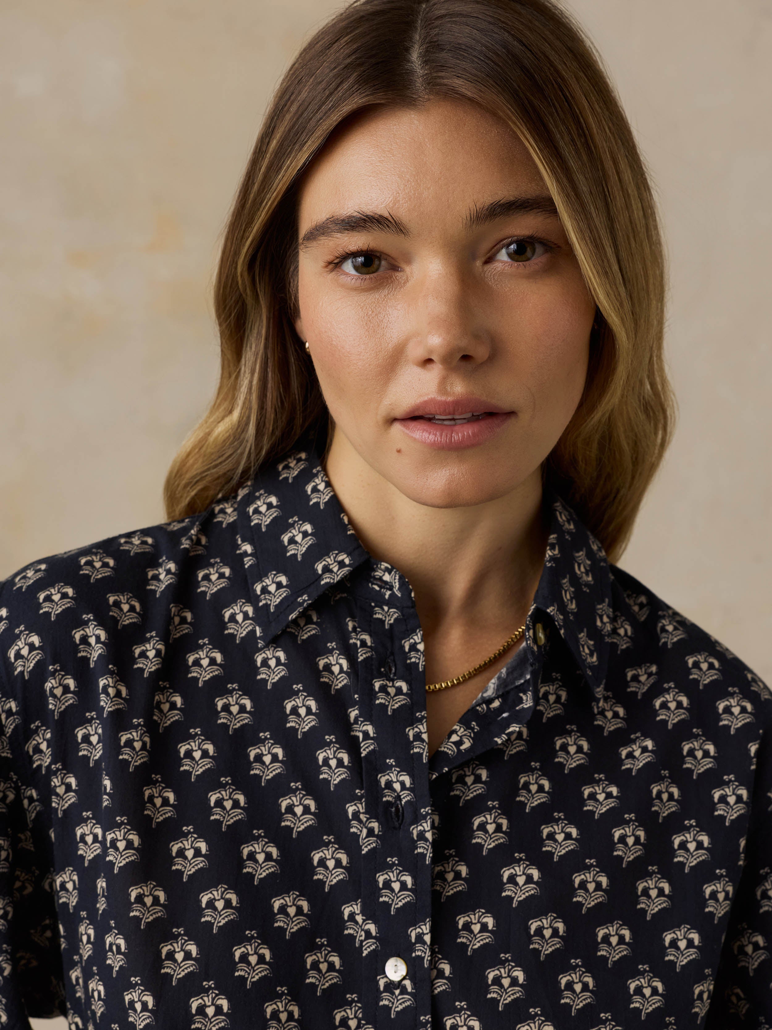 Woman wearing a dark patterned blouse against a beige background