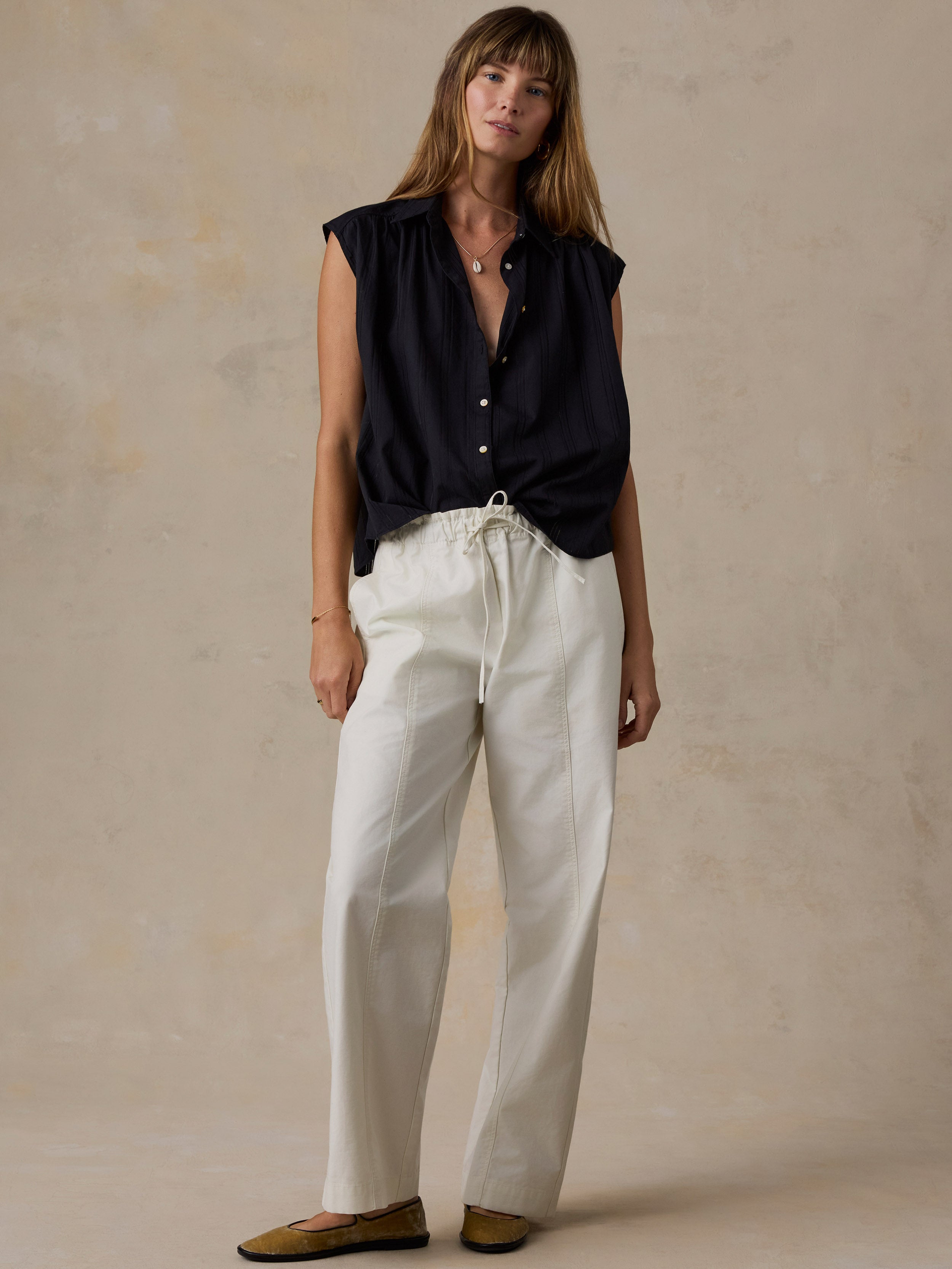 Woman wearing a black shirt and white pants against a beige background