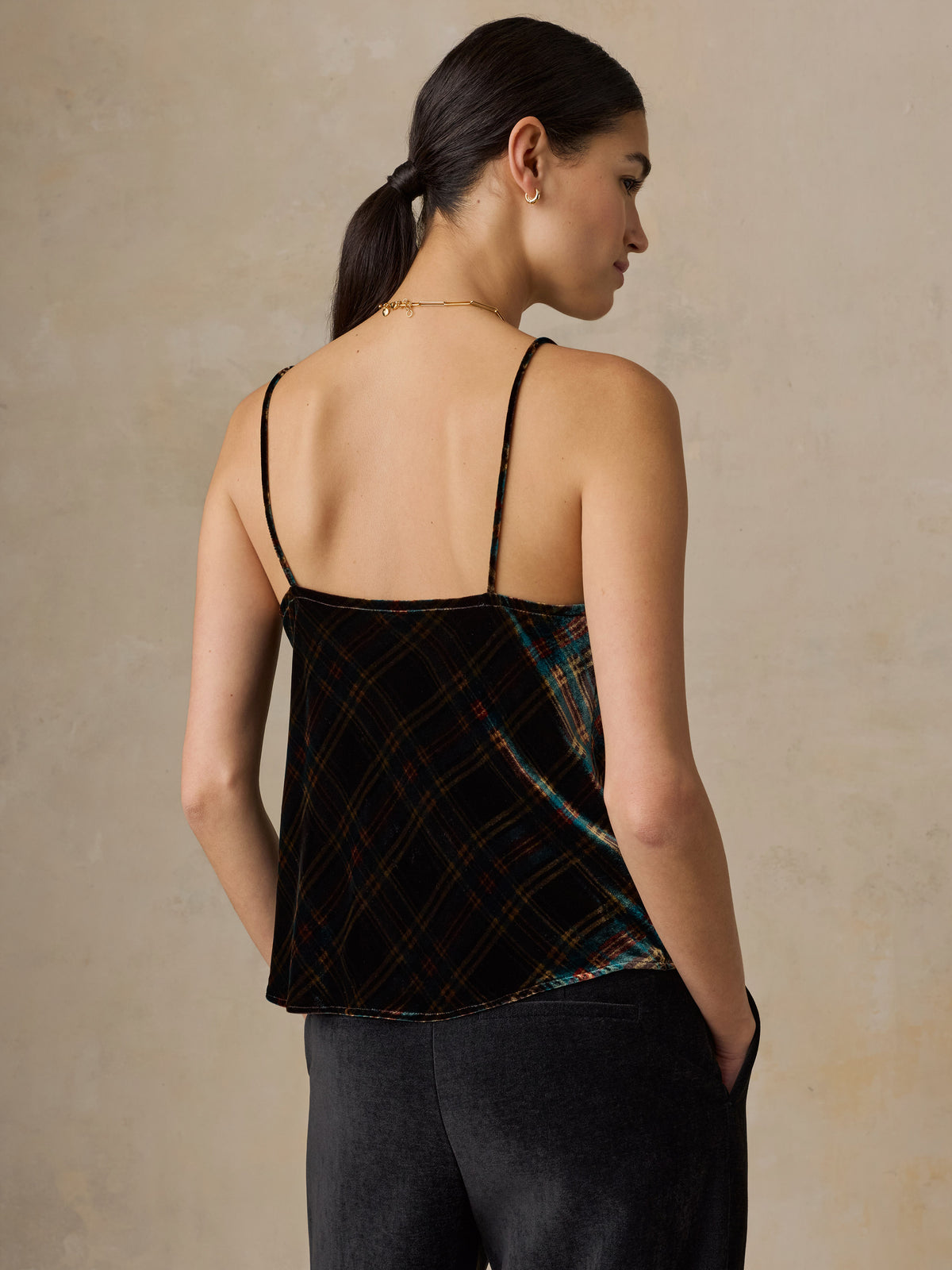 A woman viewed from behind wearing a plaid velvet top and black pants, image 2 of 5