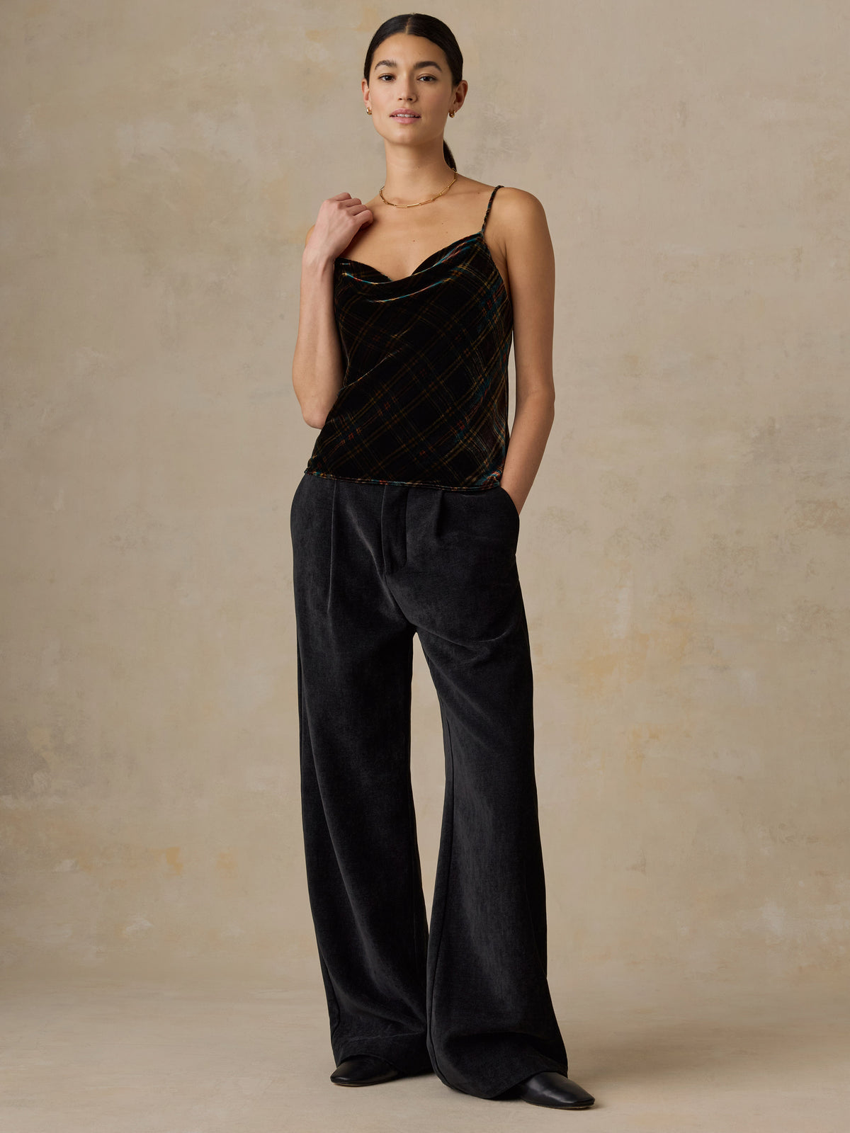A woman wearing a plaid velvet tank top and black pants, image 5 of 5
